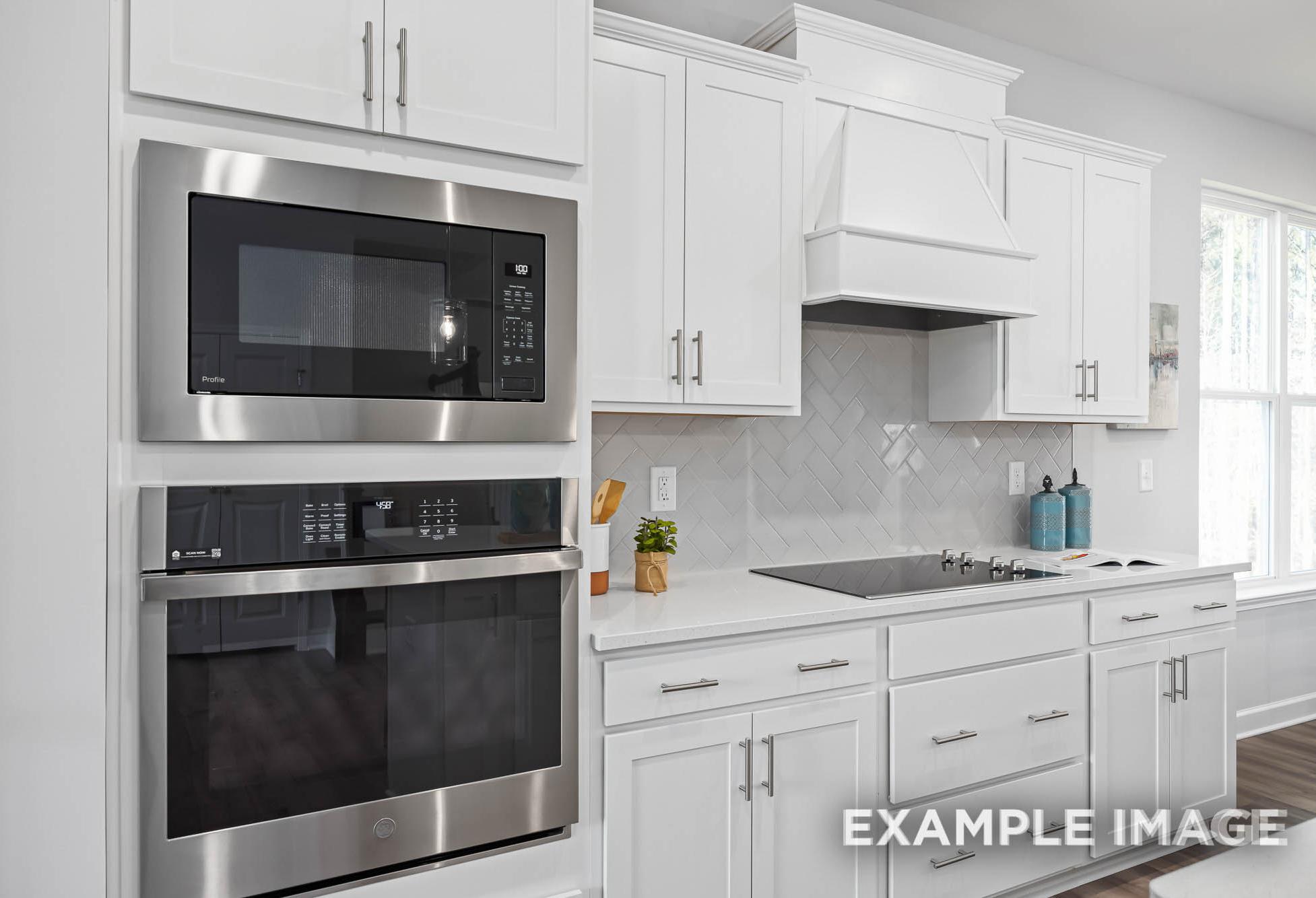 Spacious kitchen in The Ash by Davidson Homes featuring white shaker cabinets, stainless steel double oven, and subway tile backsplash