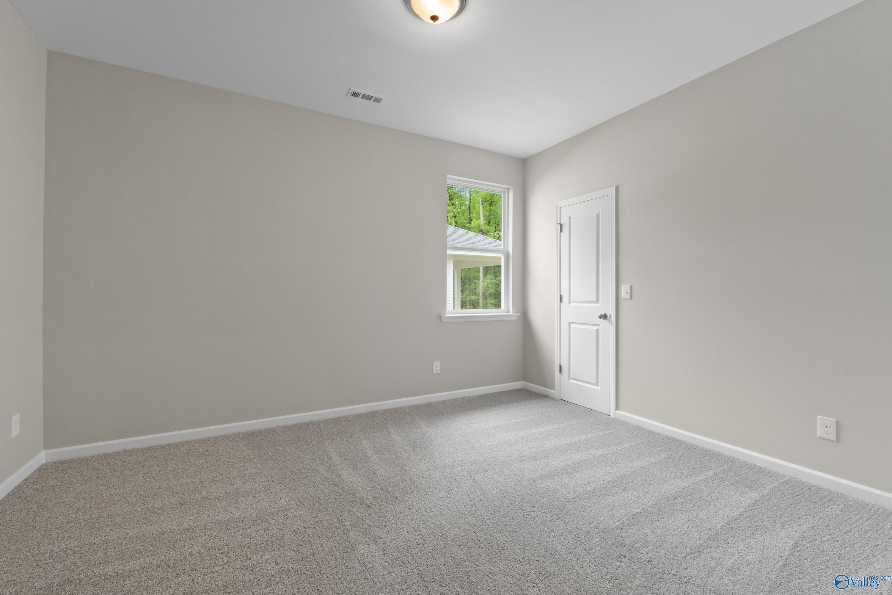 Spacious secondary bedroom with neutral gray walls, carpet floor, and window view in Davidson Homes The Luna, Hazel Green, Alabama