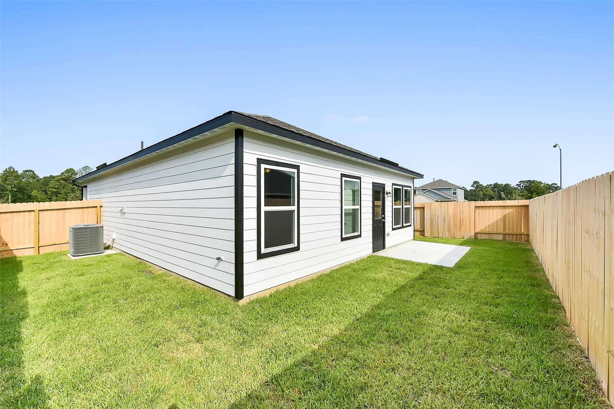 White single-story home exterior with black trim, side door, and fenced grassy backyard in The Villages at WestPointe, Dayton, Texas