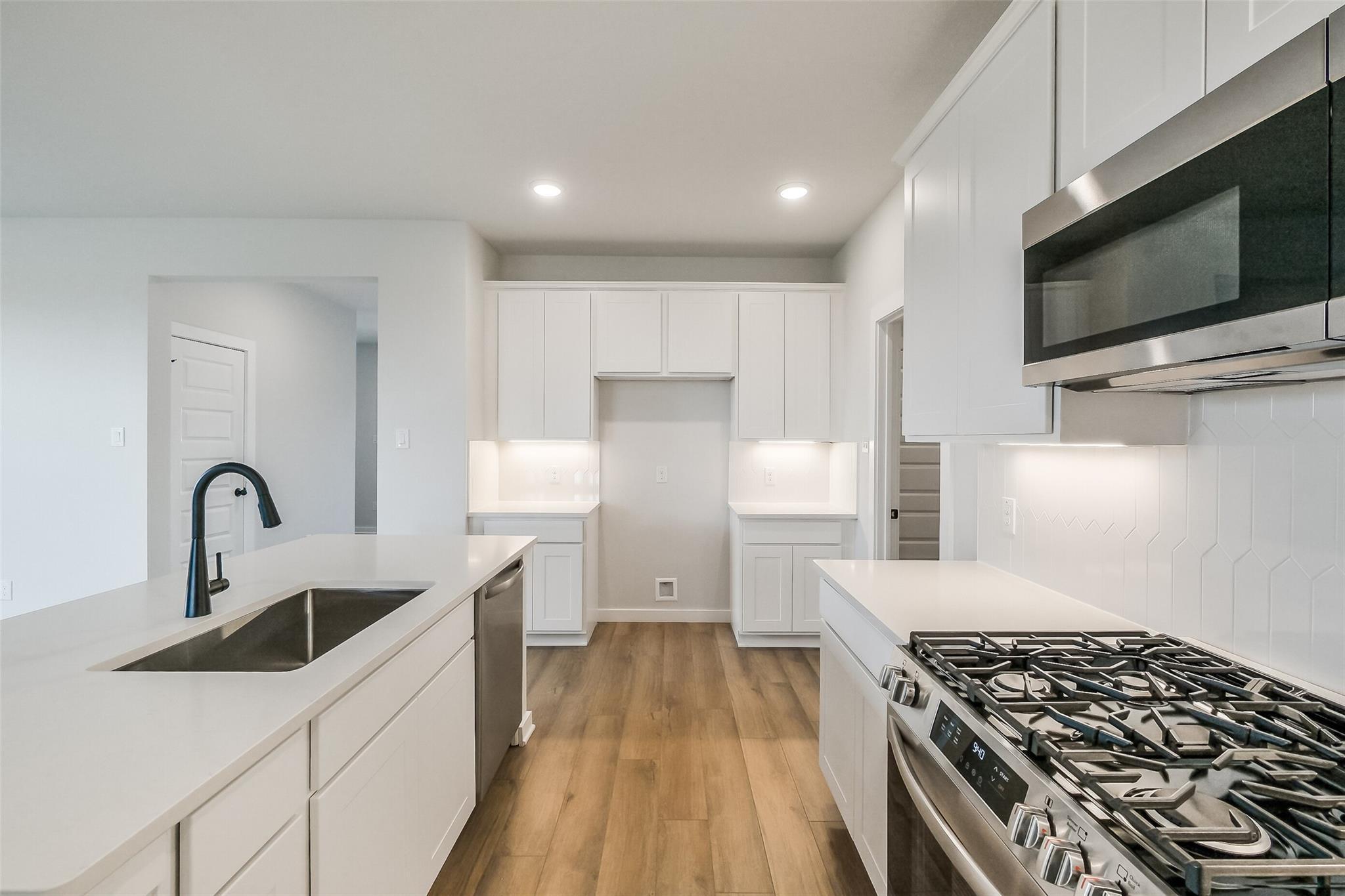 Modern white shaker kitchen with quartz island, stainless gas range, and open layout in Davidson Homes The Tierra B, Beasley, Texas
