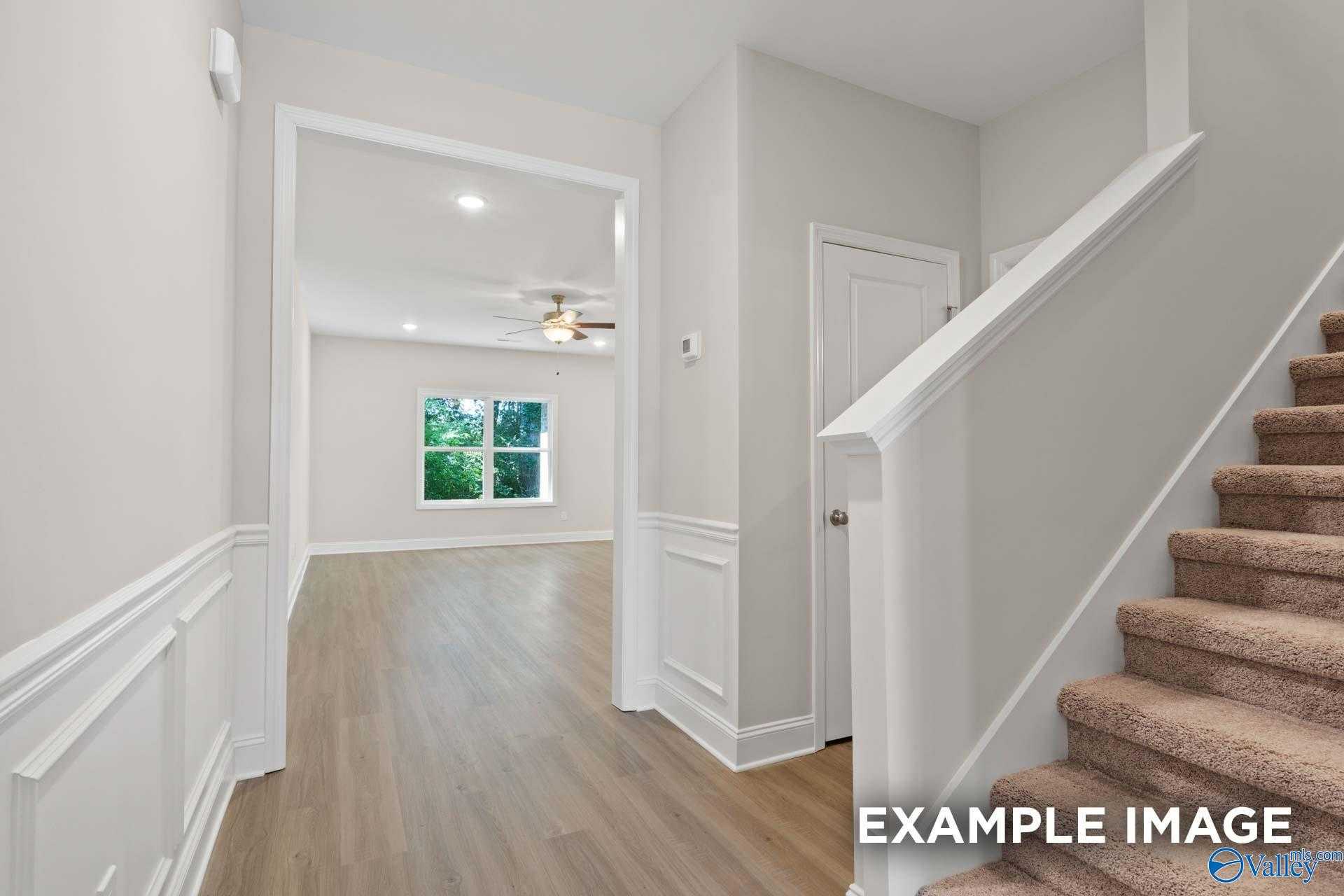 Bright foyer featuring curved wooden staircase, neutral walls, and window with lush greenery in Davidson Homes The Camden C, Huntsville AL