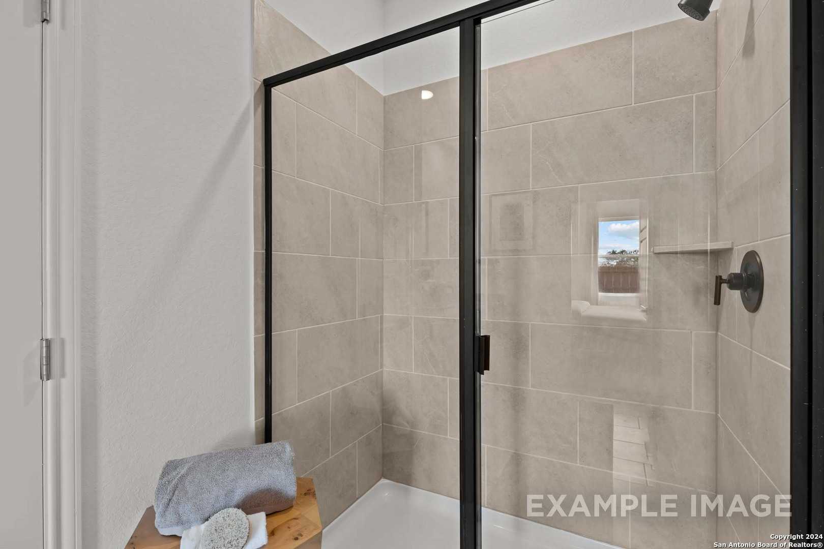 Modern frameless glass shower with beige subway tiles, rain showerhead, and built-in shelf in master bath of Davidson Homes The Douglas G, San Antonio