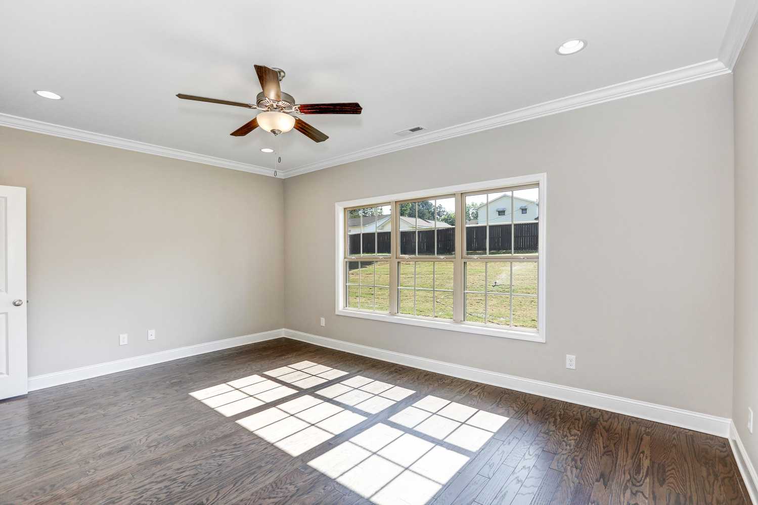 Spacious master bedroom in The Montgomery by Davidson Homes with light gray walls, hardwood floors, ceiling fan, and sunny window