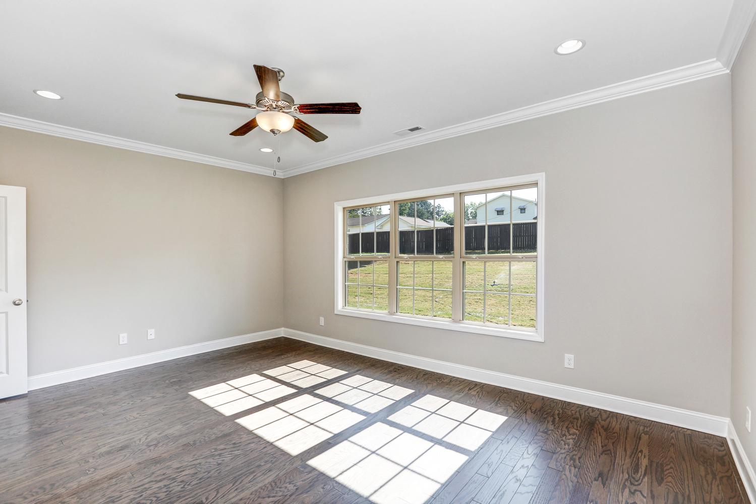 Spacious master bedroom in The Montgomery by Davidson Homes with light gray walls, hardwood floors, ceiling fan, and sunny window