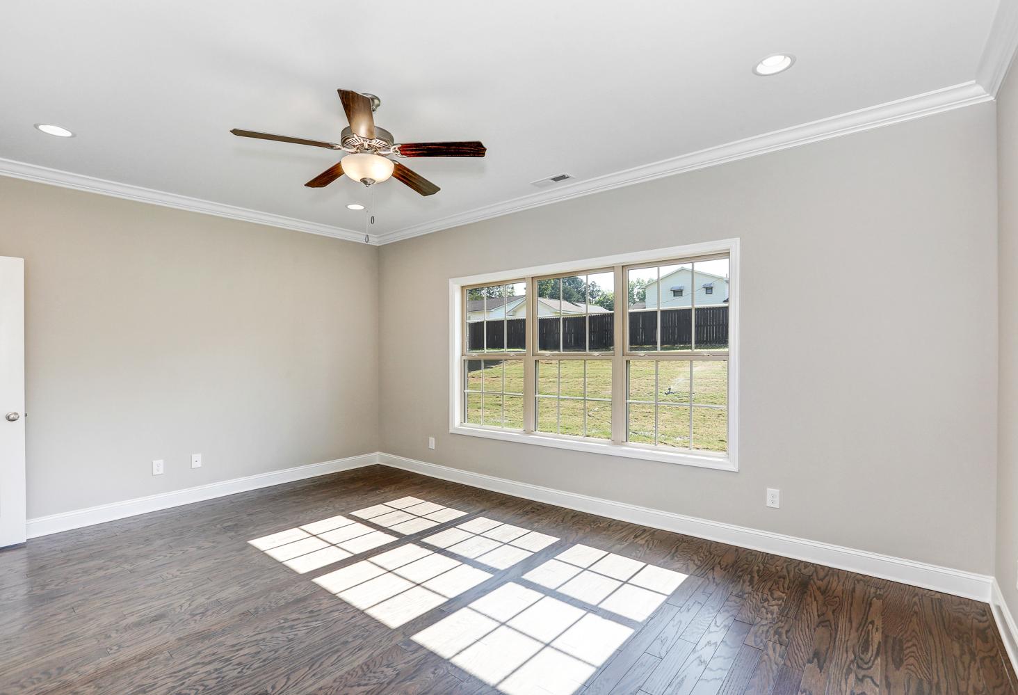 Spacious master bedroom in The Montgomery with light gray walls, hardwood floors, large triple windows, and ceiling fan