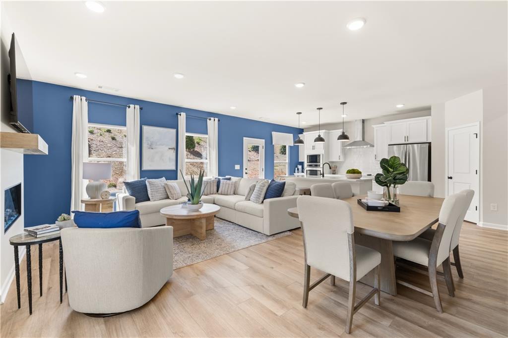 Open-concept living room with blue accent wall, gas fireplace, beige sectional sofa, and adjacent kitchen in Davidson Homes The Burton C, Canton, Georgia