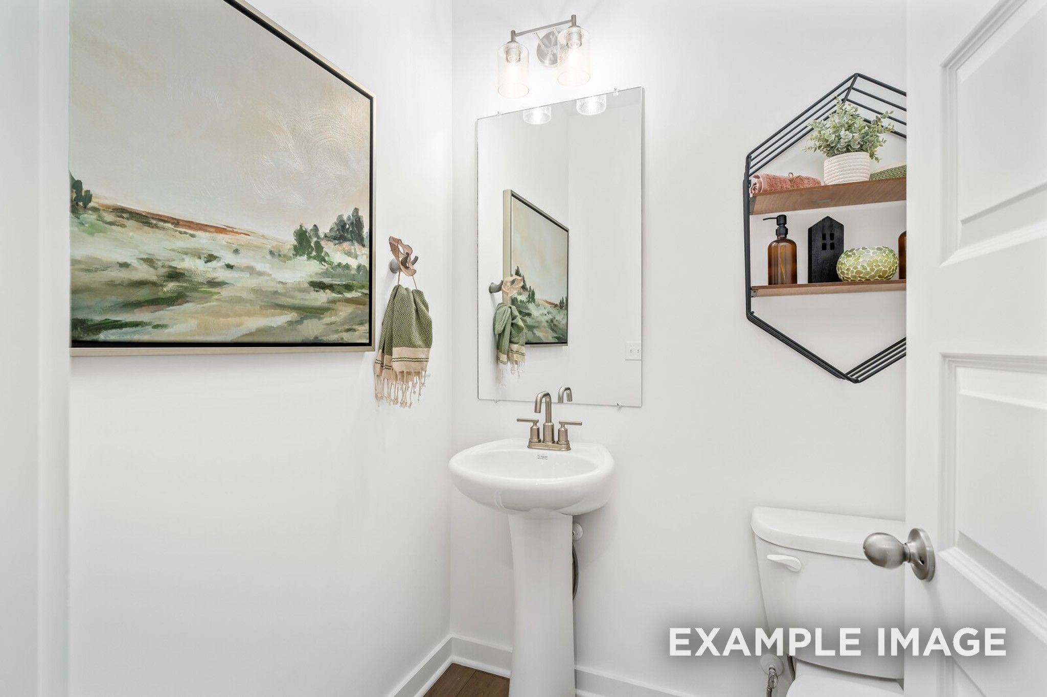 Elegant powder room with pedestal sink, round mirror, abstract landscape art, and hexagonal shelf in Davidson Homes The Ash A, Gallatin, Tennessee