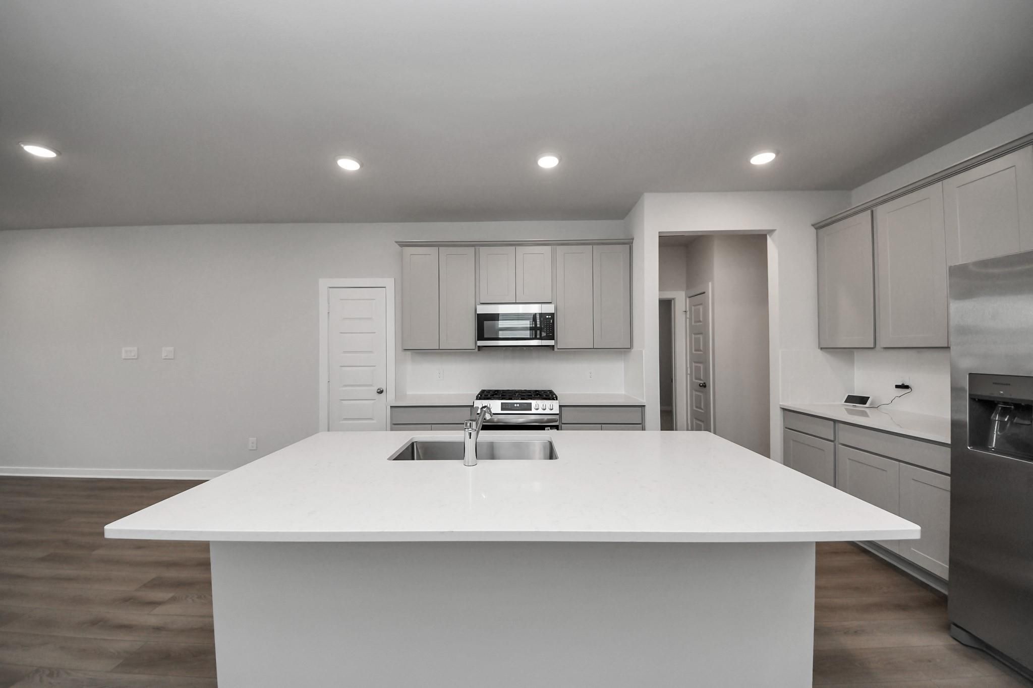 Modern kitchen with large island, stainless appliances, and gray cabinetry in The Frio F floor plan at Robins Landing, Houston.