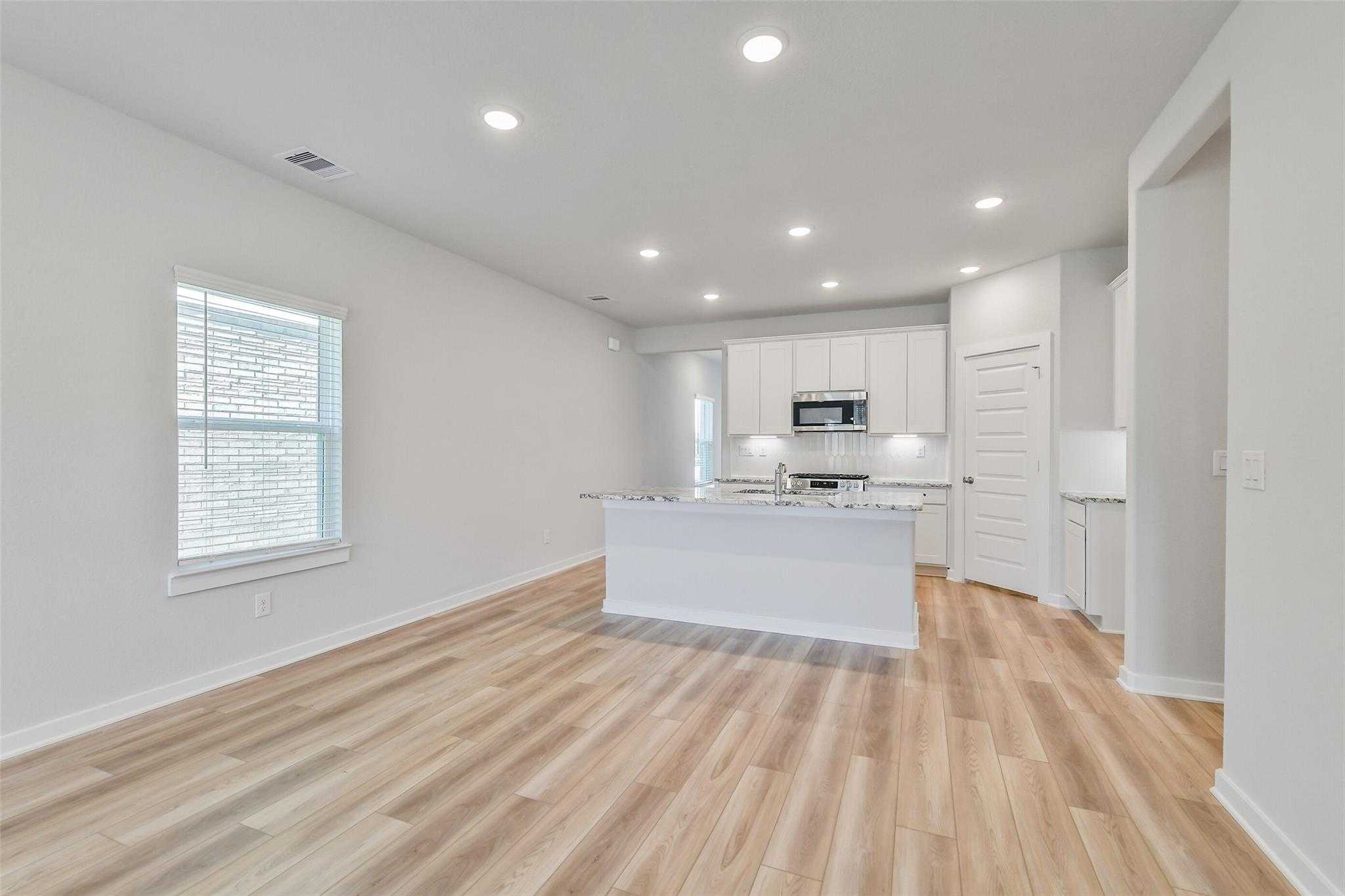 Modern open-concept kitchen with white shaker cabinets, large island, stainless appliances, and hardwood floors in 5-bedroom Davidson Homes Rio Grande H, Magnolia TX