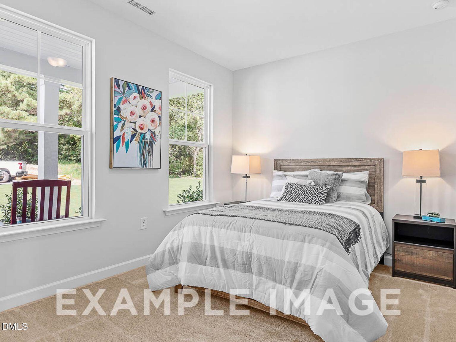 Bright secondary bedroom with queen bed, striped bedding, lamps, floral wall art, and yard views in Davidson Homes The Chestnut B, Lillington NC