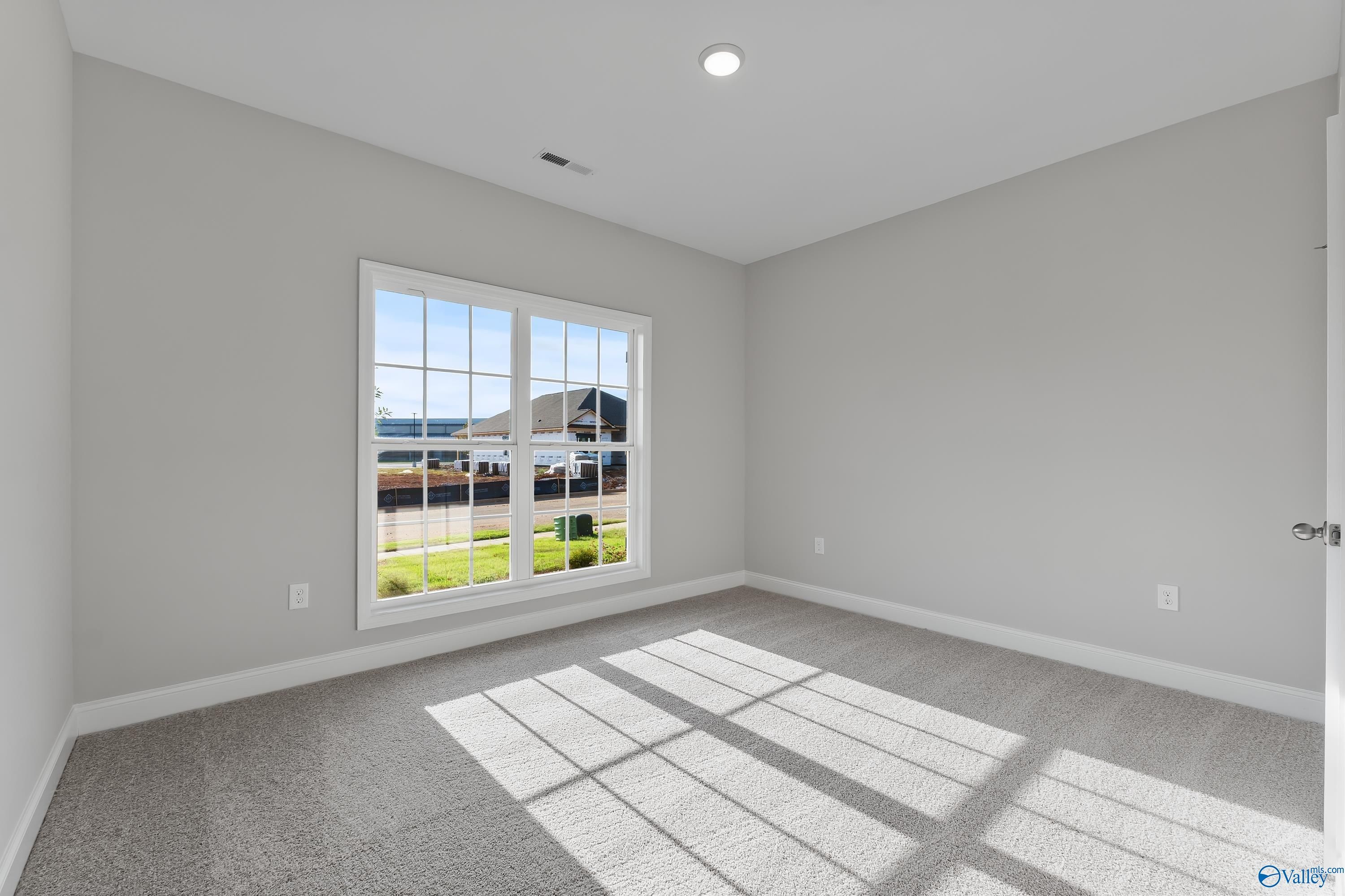 Bright secondary bedroom with gray walls, large window overlooking green lawn, and carpeted floor in Davidson Homes The Daphne C, Huntsville