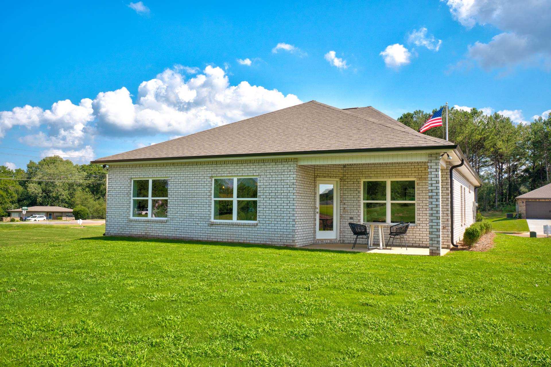 Brick ranch home exterior at Blue Spring in Huntsville AL by Davidson Homes, featuring covered porch, American flag, and lush green yard