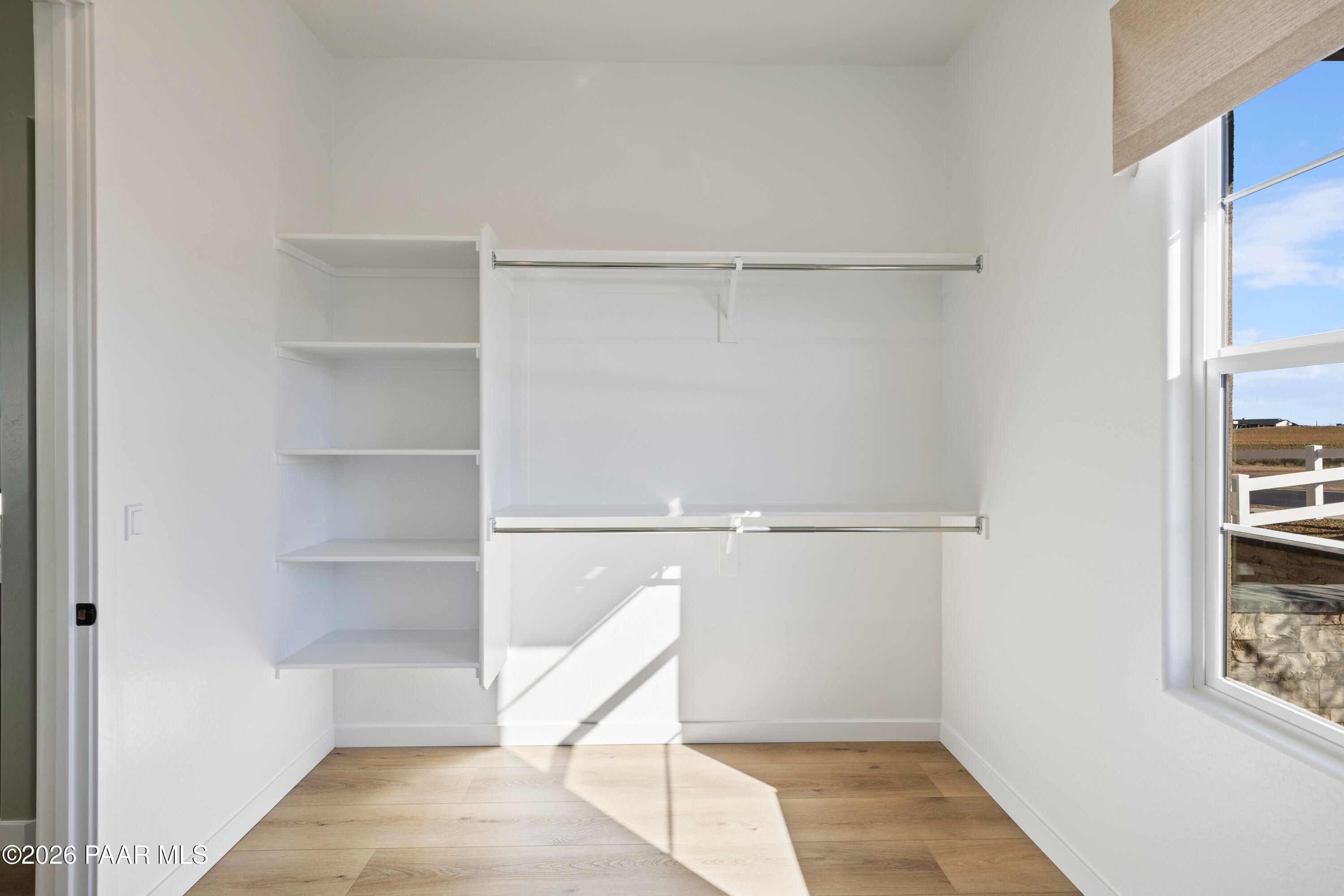 Walk-in closet with built-in shelving, hanging rods, and wood flooring in The Blaze D floor plan at Hidden Hills, Prescott.