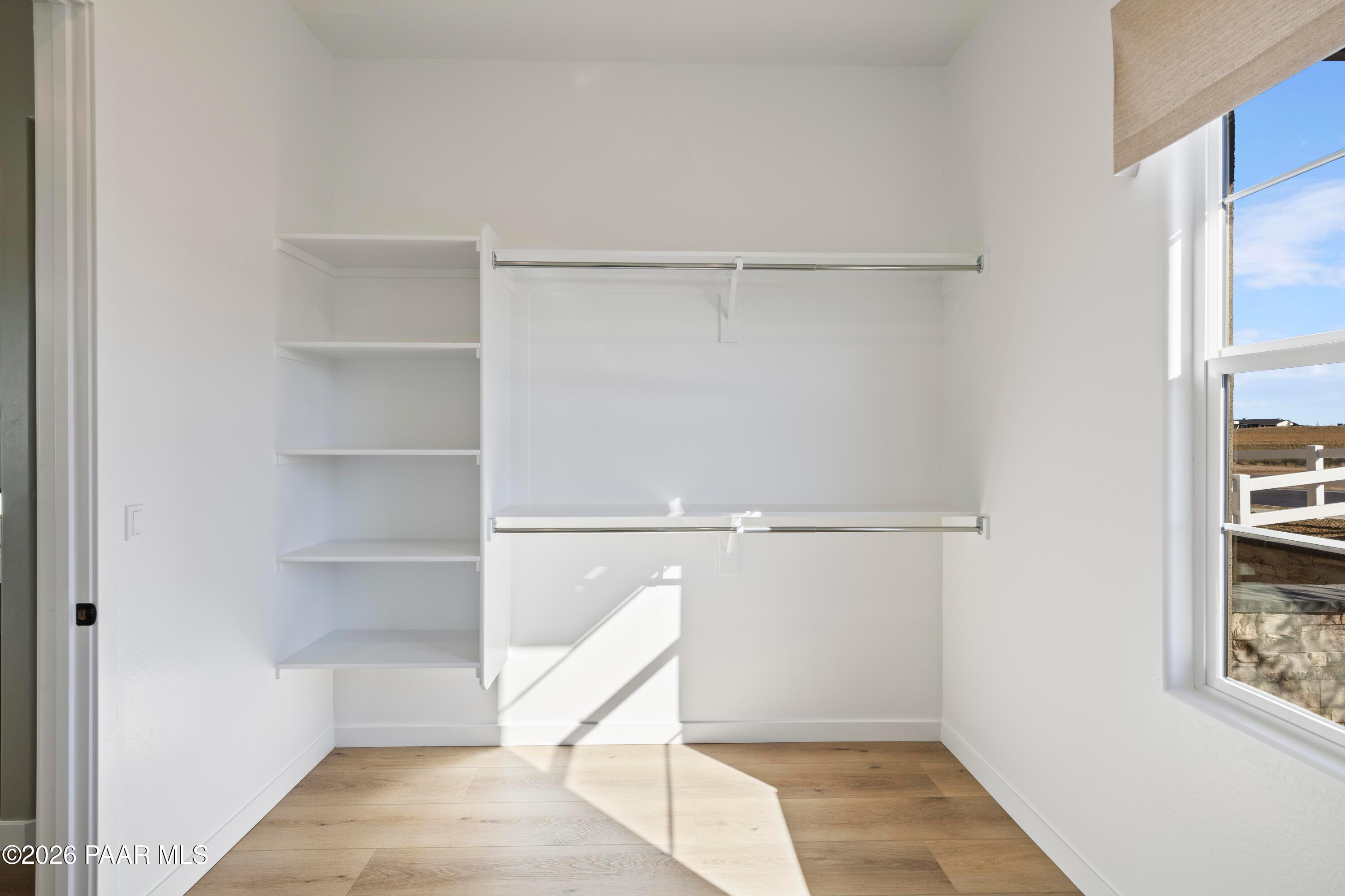 Walk-in closet with built-in shelving, hanging rods, and wood flooring in The Blaze D floor plan at Hidden Hills, Prescott.