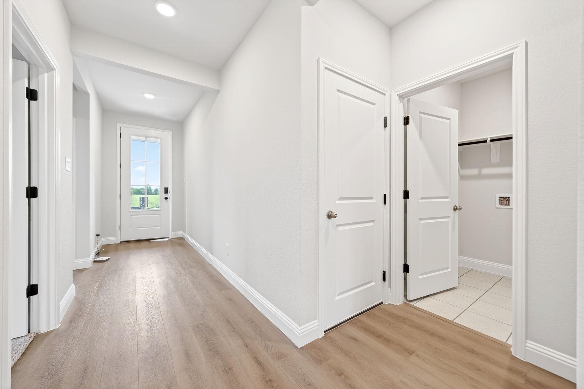 Bright entryway and laundry room in The Redbud floor plan by Davidson Homes, featuring wood-look flooring and white doors.