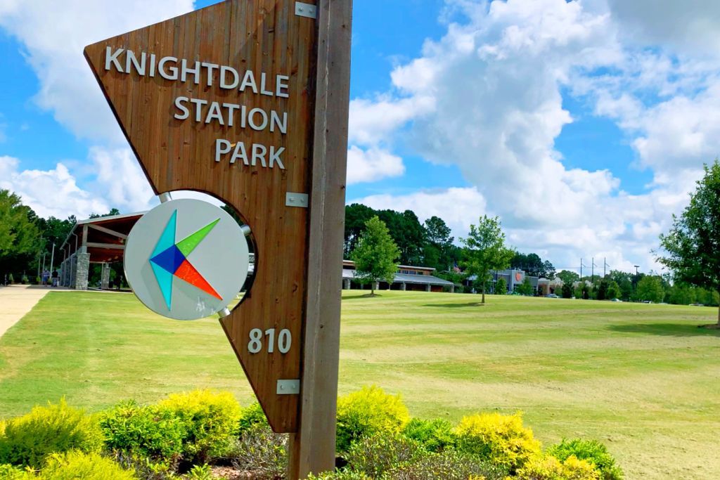 Knightdale Station Park sign with wooden post, logo, and address 810 amid green lawns, trees, and modern pavilion in Knightdale NC