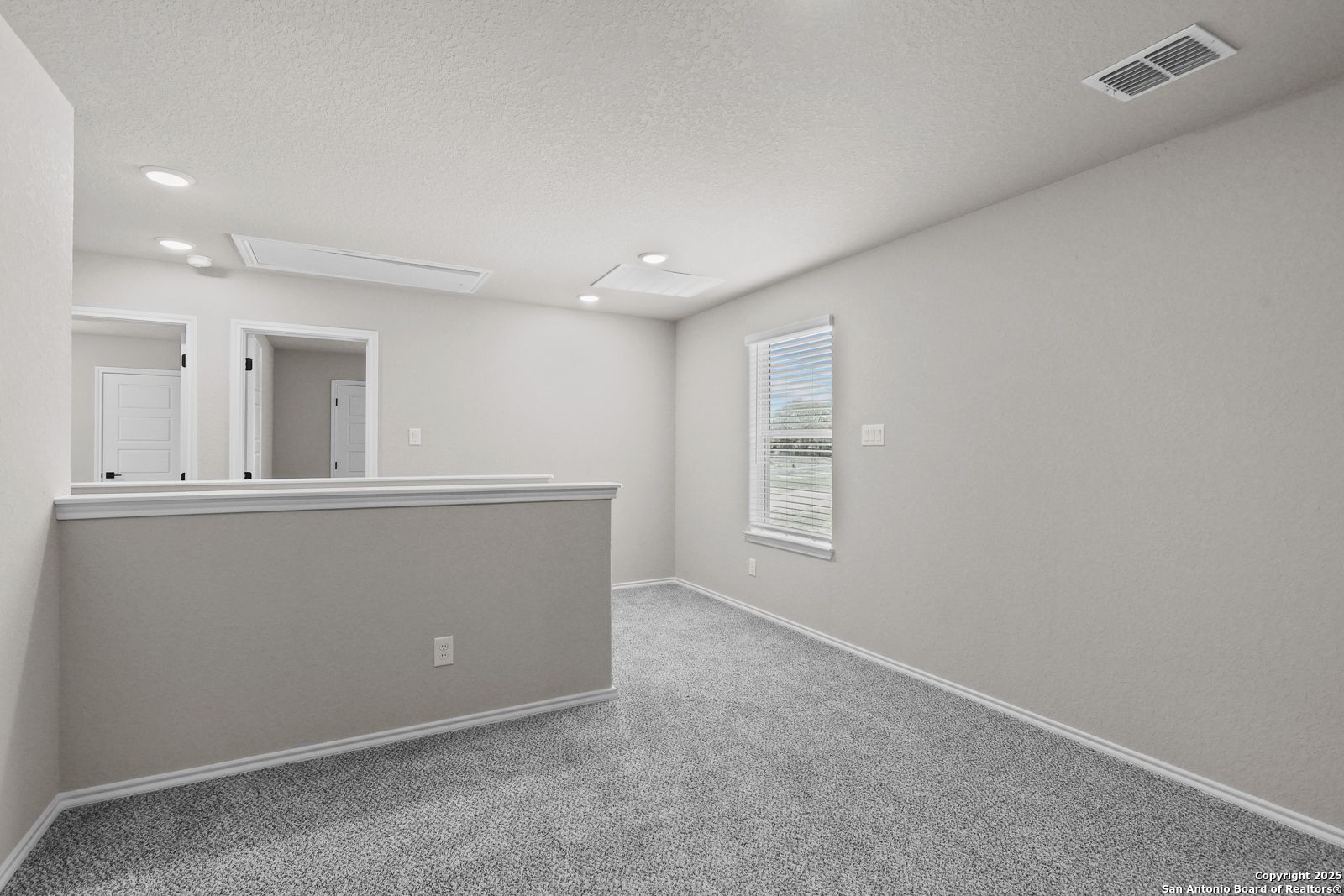 Spacious upstairs loft with beige walls, carpet floor, balcony railing, and window in Davidson Homes The Charlotte B, San Antonio