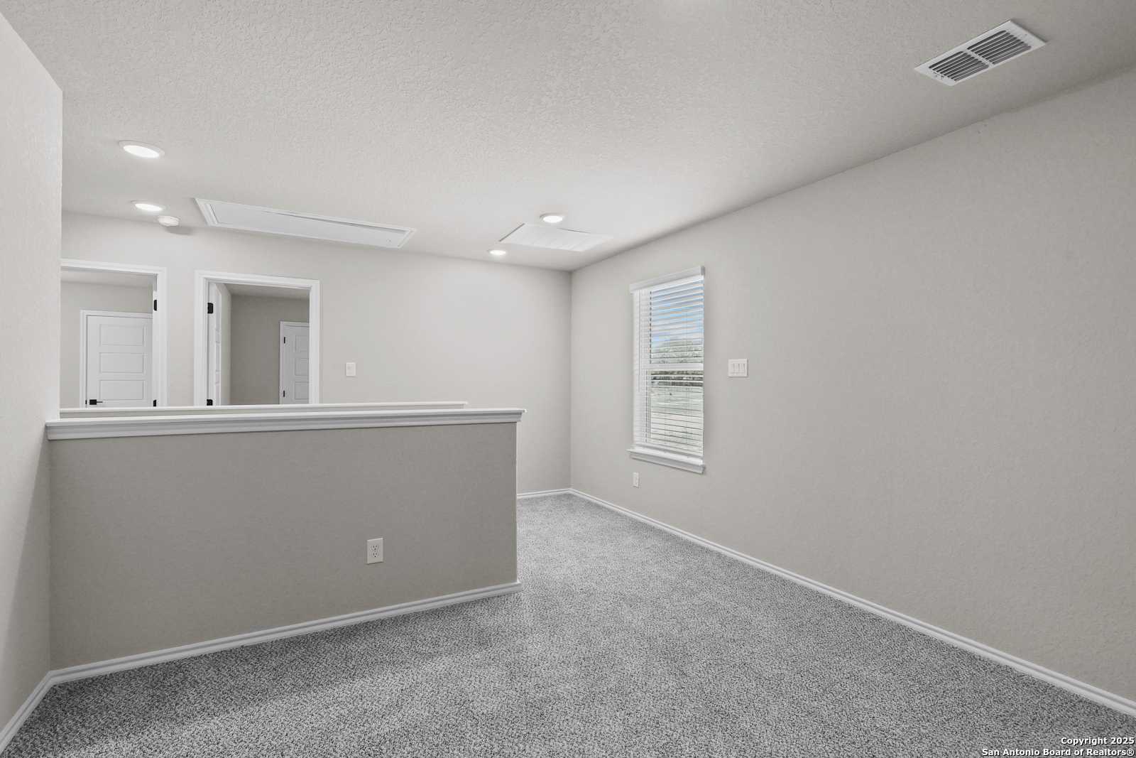 Spacious upstairs loft with beige walls, carpet floor, balcony railing, and window in Davidson Homes The Charlotte B, San Antonio
