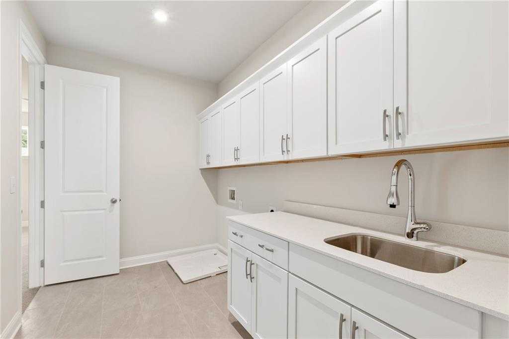 Modern laundry room with white shaker cabinets, utility sink, and washer-dryer space in Davidson Homes The Hampton C, Buford, Georgia