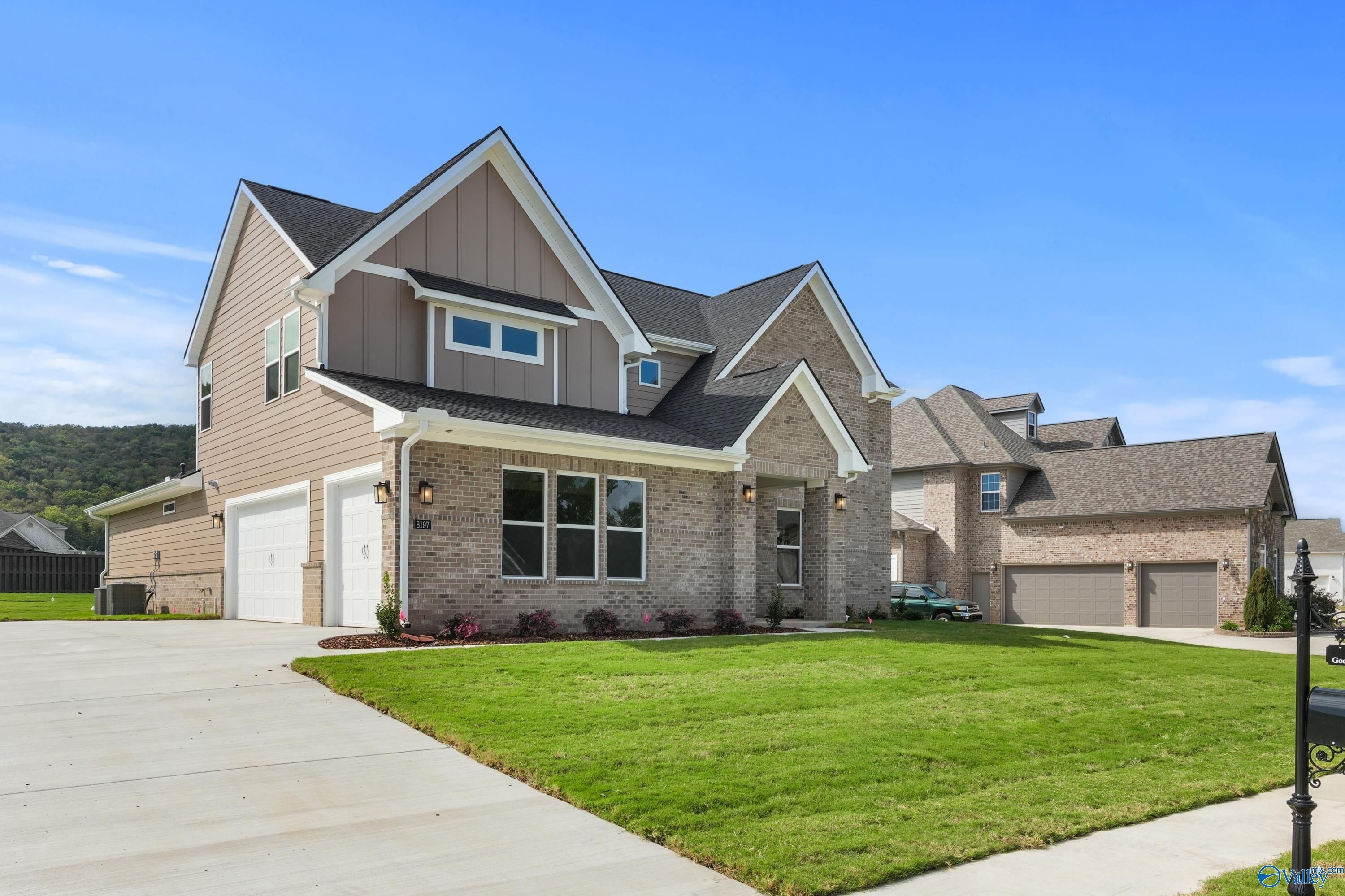 Modern two-story beige brick home with 3-car garage, driveway, lush green lawn in The Meadows at Hampton Cove, Owens Cross Roads, Alabama