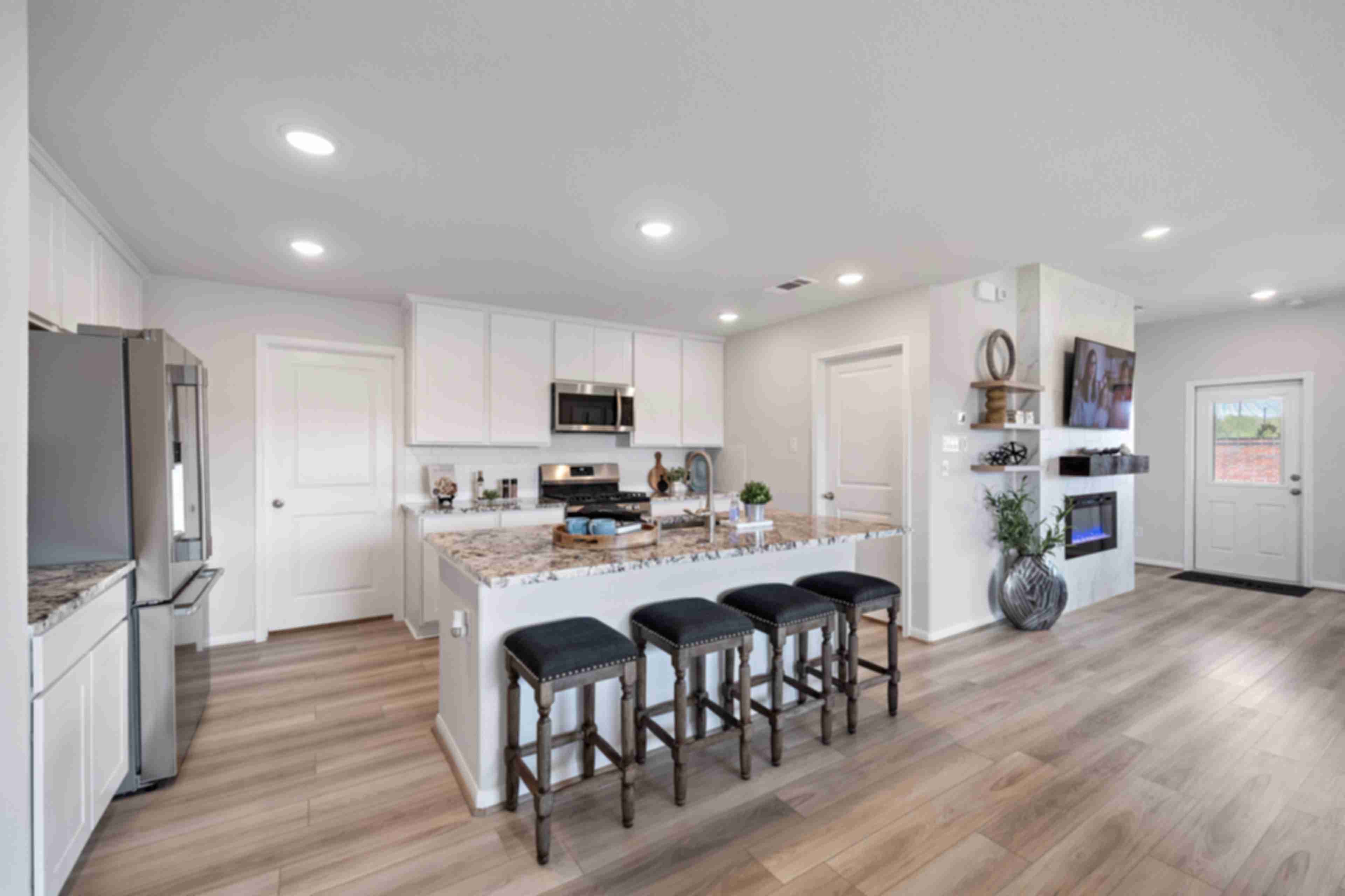 Modern open-concept kitchen in Sunterra Katy TX by Davidson Homes featuring white cabinets, granite island with bar seating, stainless appliances, hardwood floors