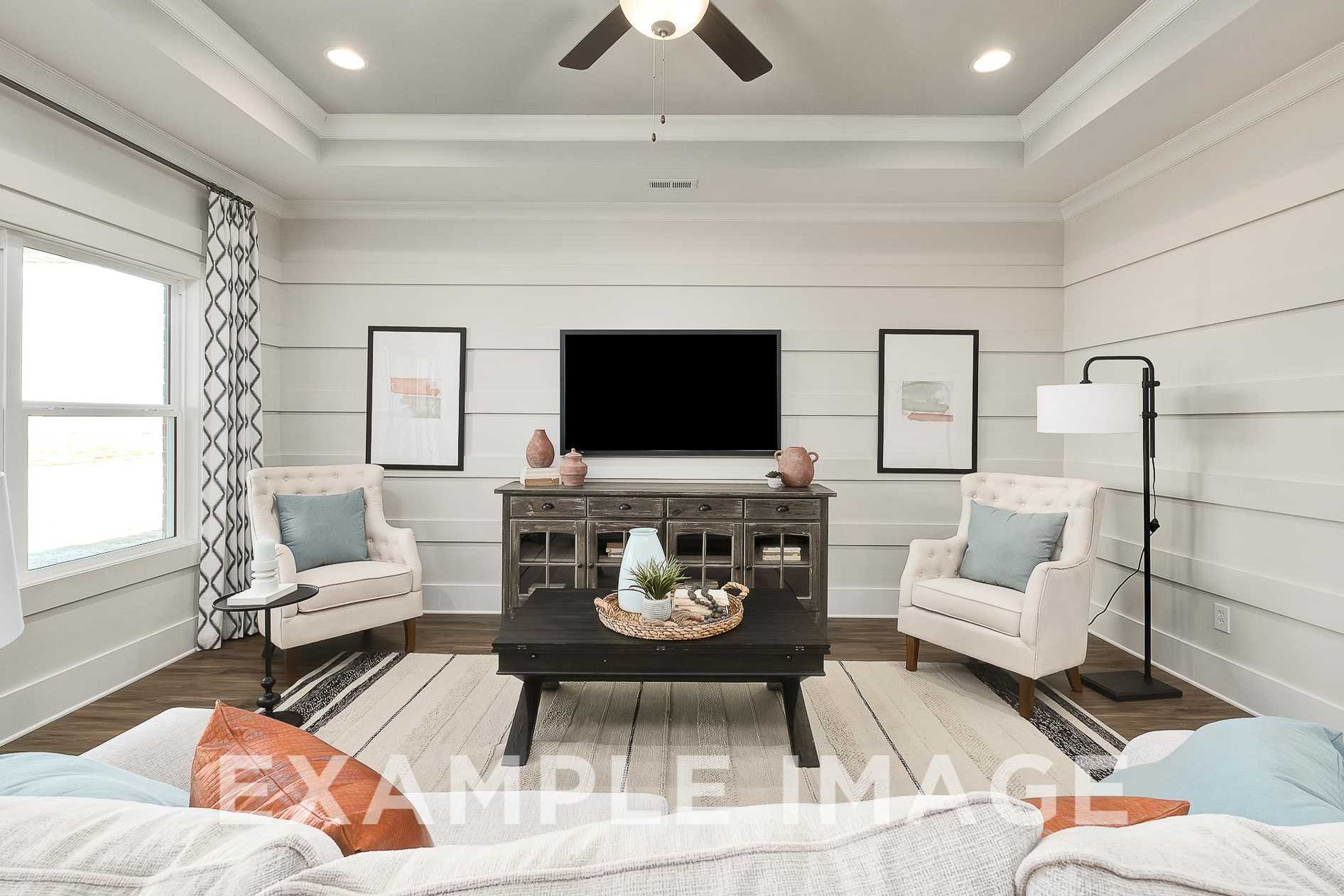 Spacious living room in The Everett B with white shiplap walls, ceiling fan, mounted TV, armchairs, and wooden tables