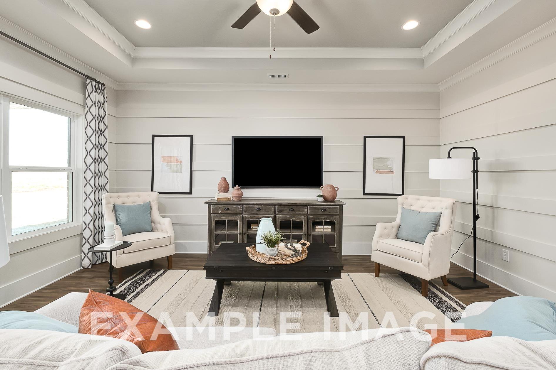 Spacious living room in The Everett B with white shiplap walls, ceiling fan, mounted TV, armchairs, and wooden tables