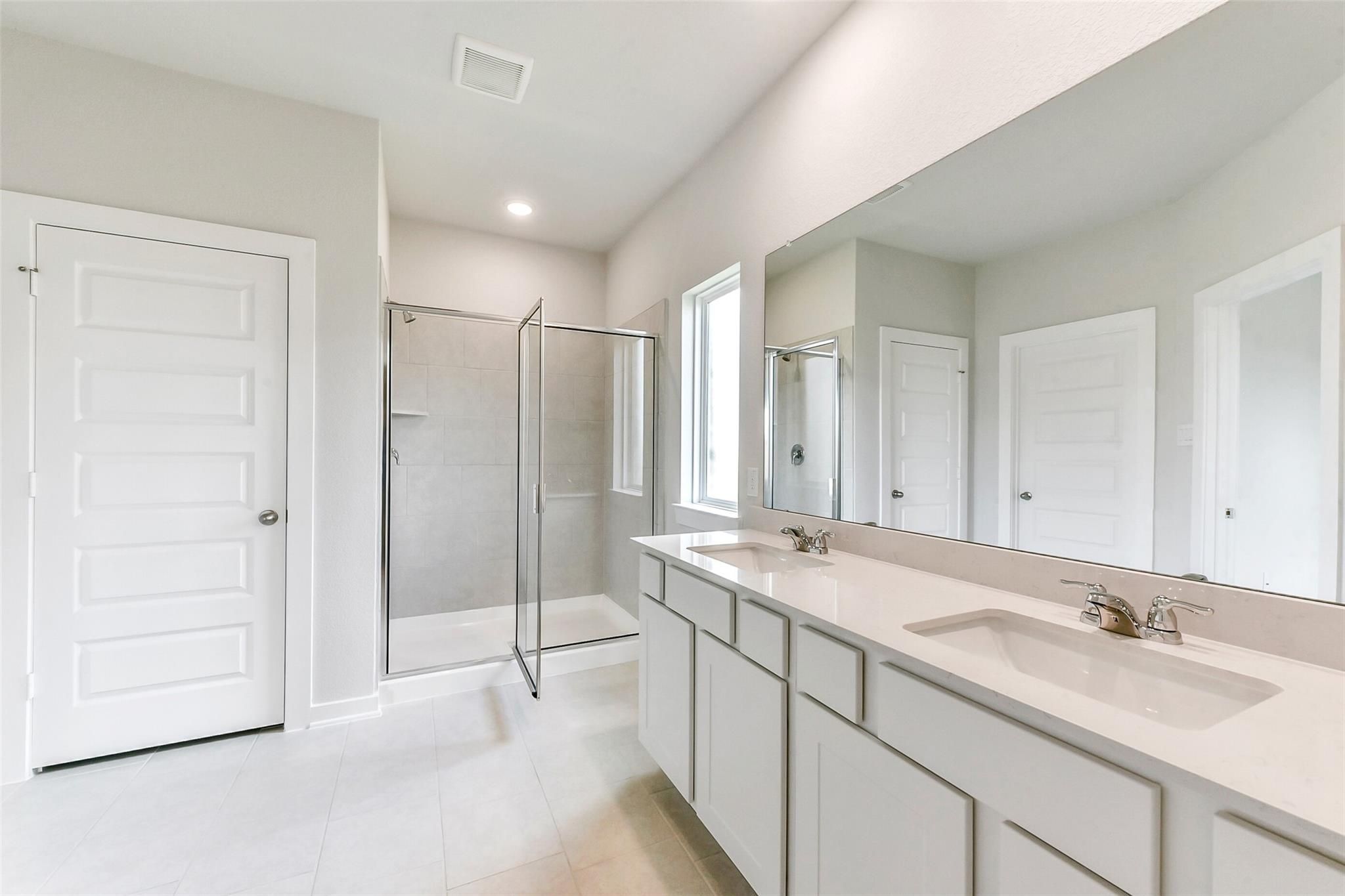 Modern master bathroom featuring double white vanity, large mirror, and glass shower enclosure in Davidson Homes The Costa B, Dayton, Texas
