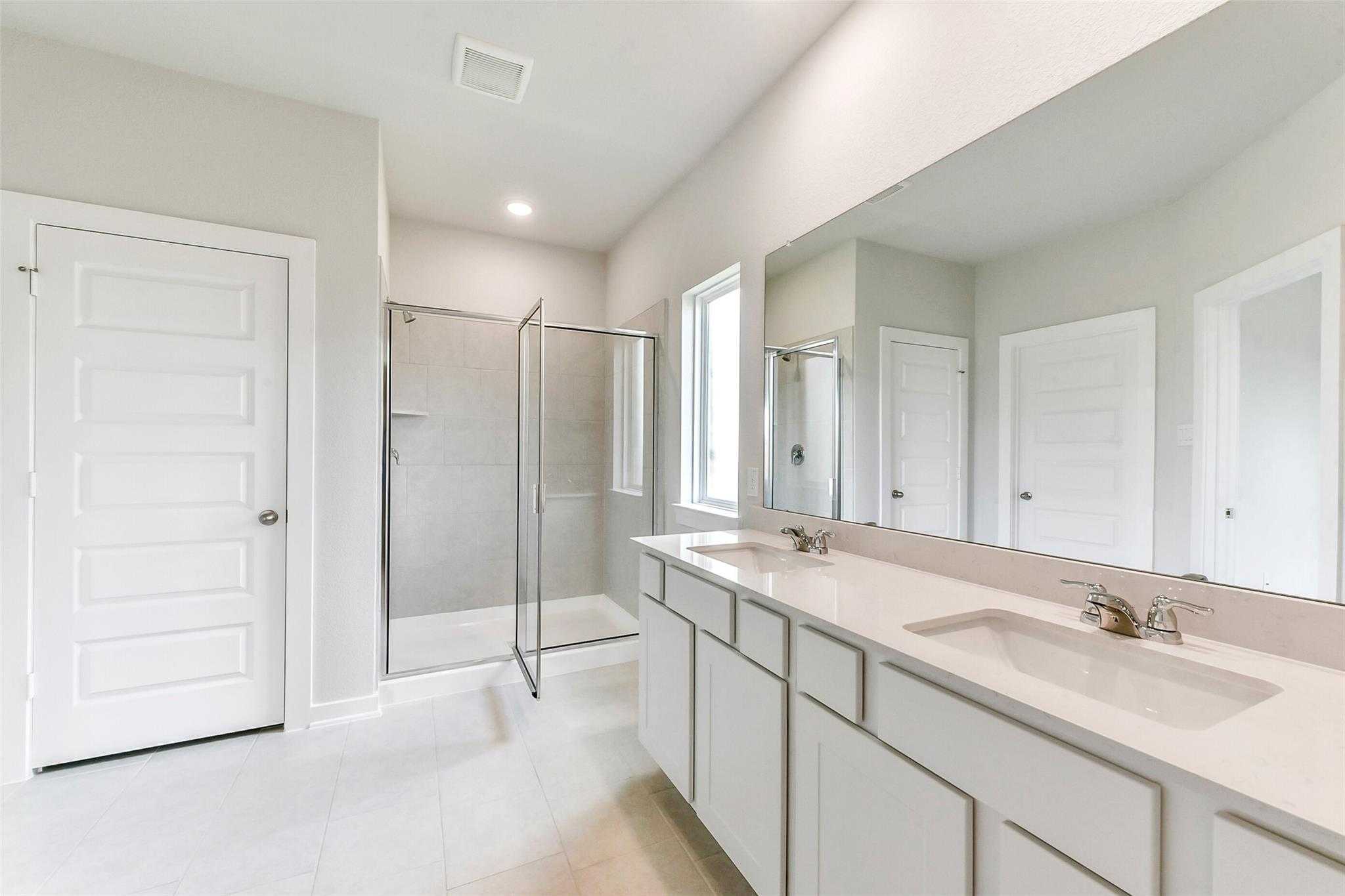 Modern master bathroom featuring double white vanity, large mirror, and glass shower enclosure in Davidson Homes The Costa B, Dayton, Texas
