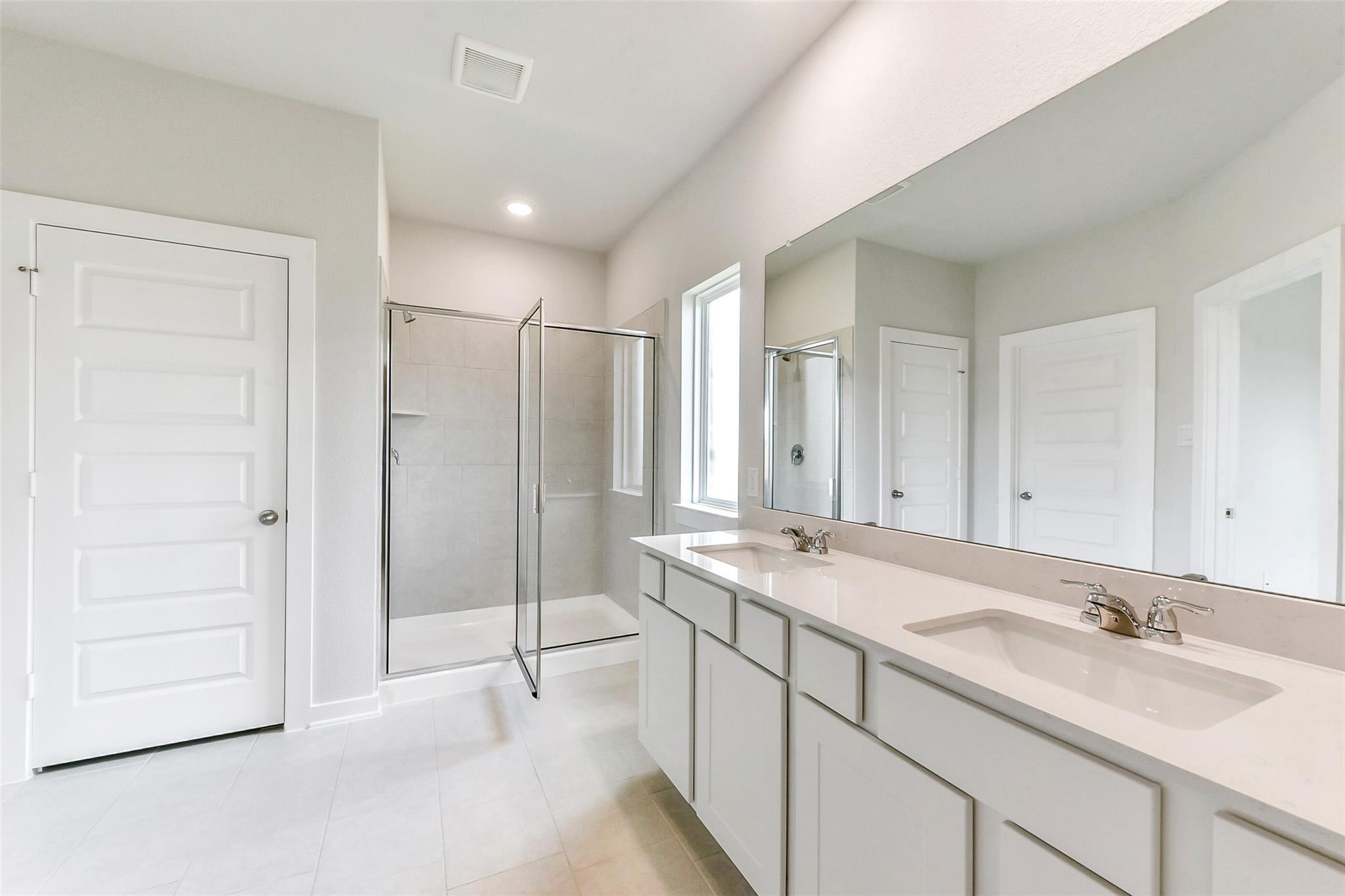 Modern master bathroom featuring double white vanity, frameless glass shower, and large mirror in Davidson Homes The Costa B, Dayton, Texas