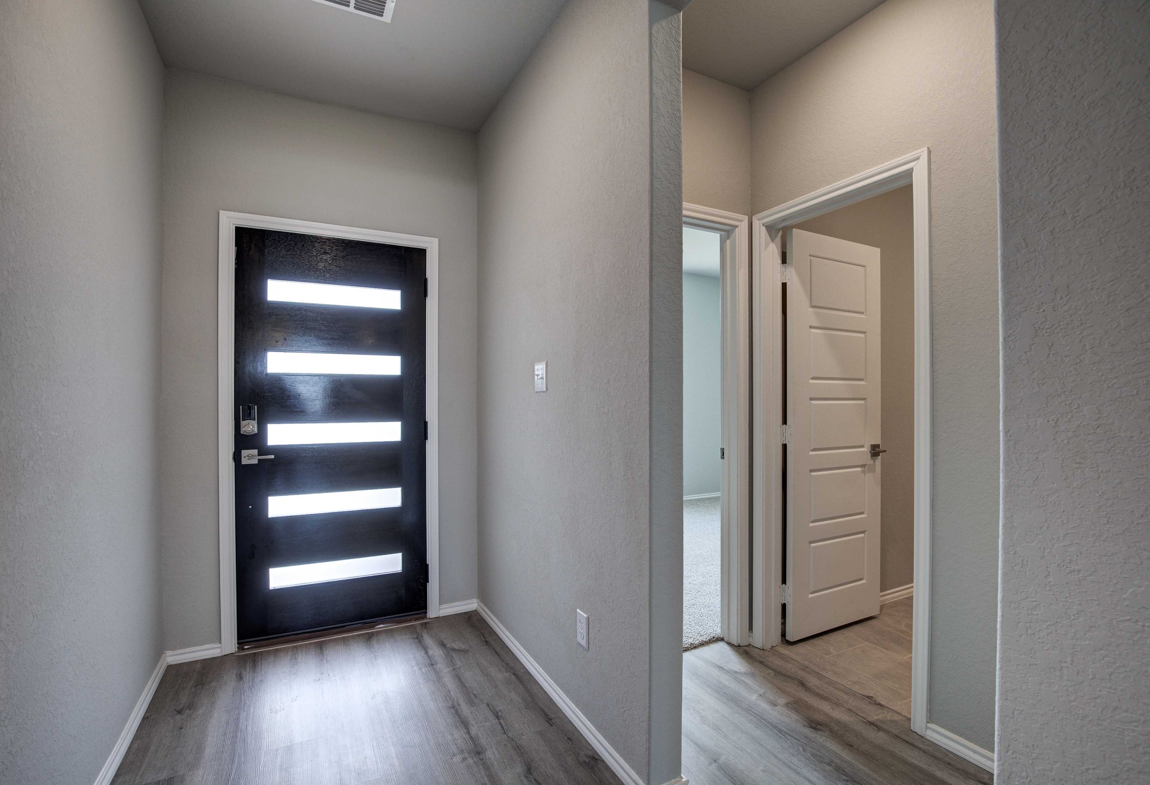 Modern entryway in The Asheville home design with sleek black front door, frosted glass panels, neutral walls, light wood floors