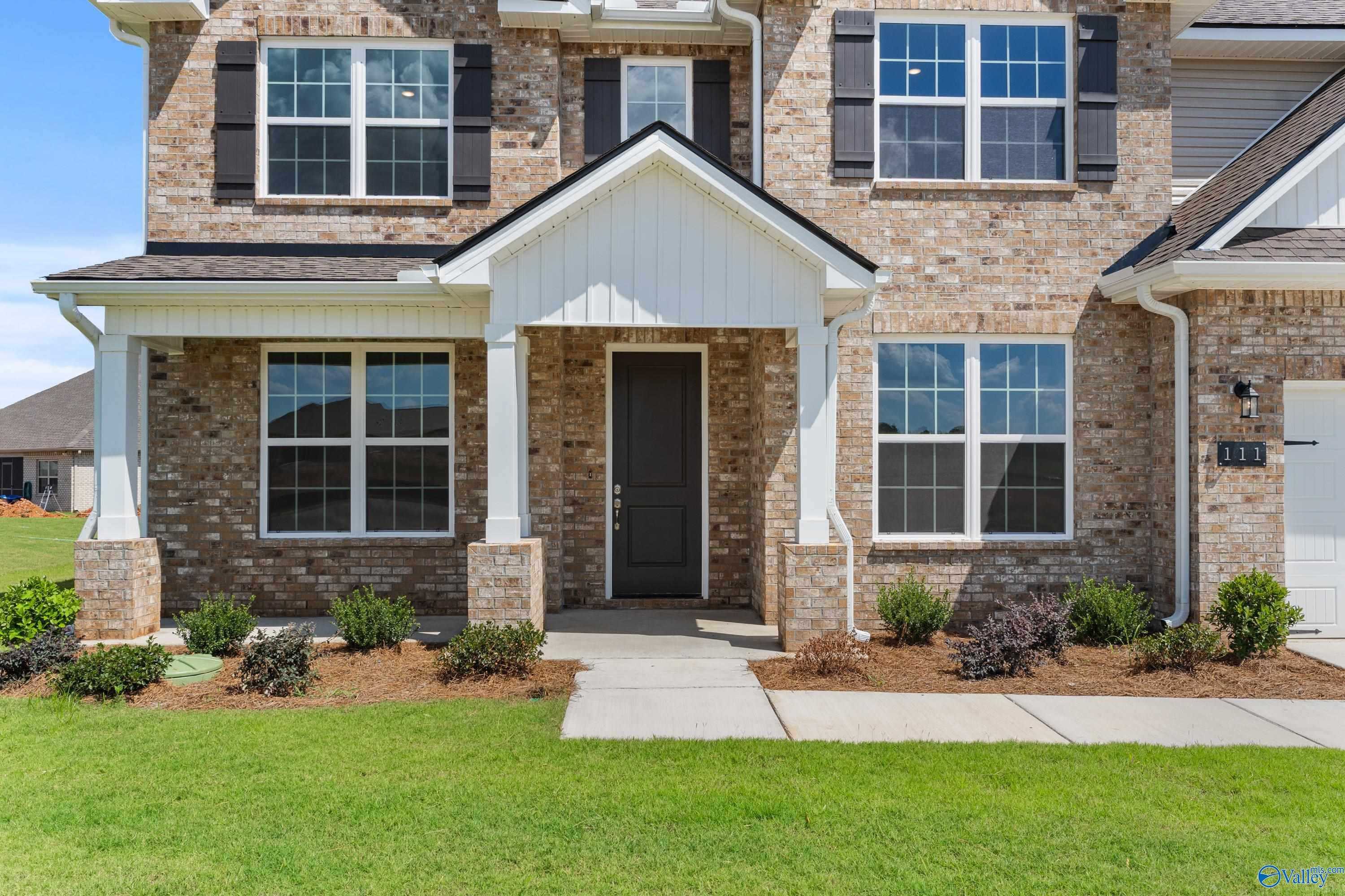 Two-story brick home with white-columned front porch, black shutters, garage, and lush landscaping in Pikes Ridge, Meridianville, Alabama