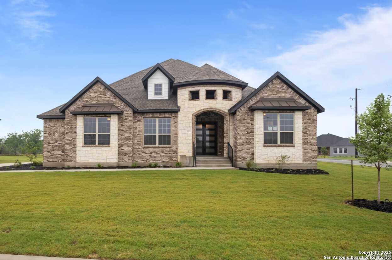 Elegant stone and stucco single-story home exterior with arched entry, large windows, and lush green lawn in Potranco Oaks, Castroville, Texas
