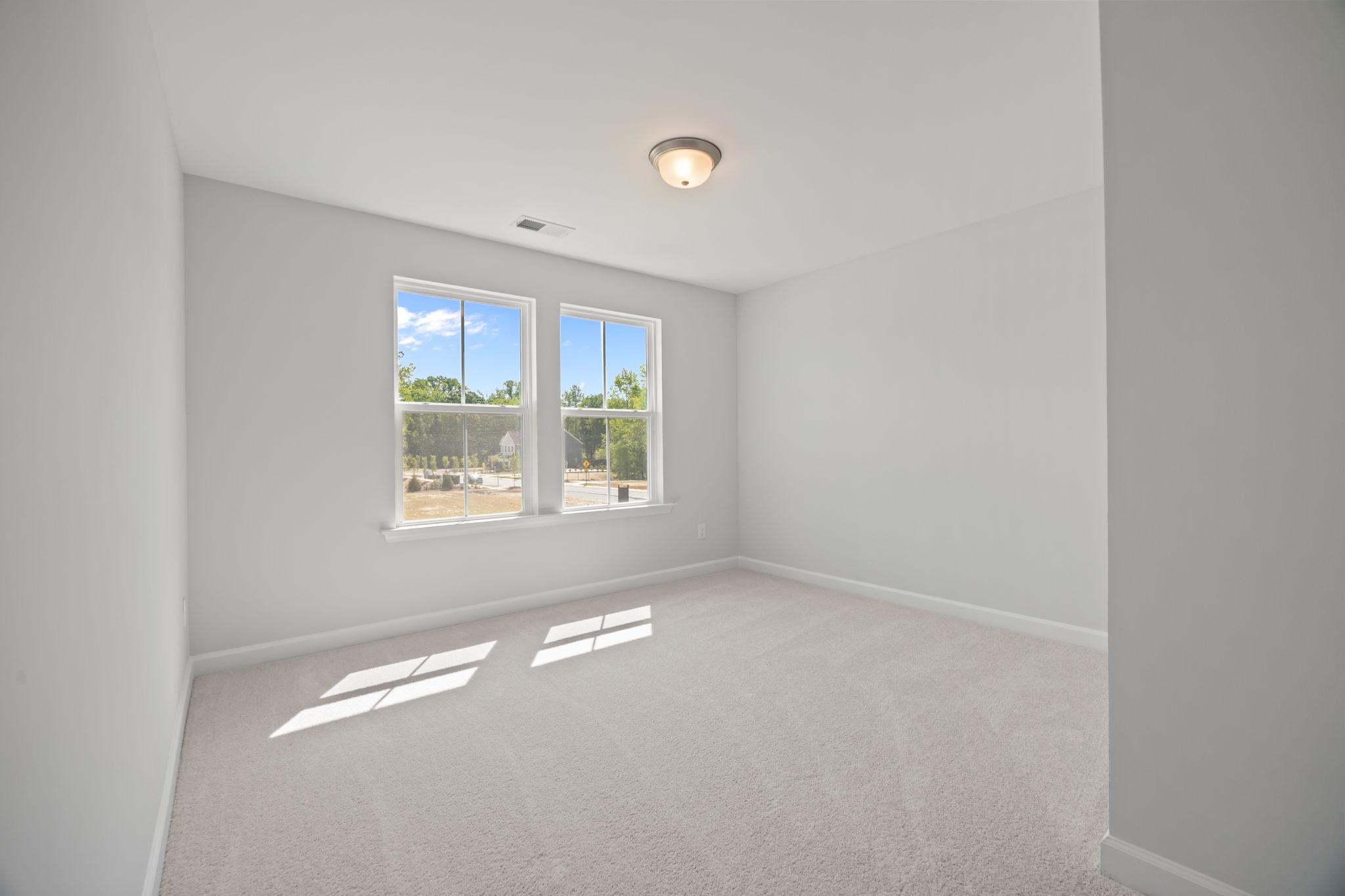 Spacious, carpeted bedroom in The Ashport B floor plan featuring neutral paint and natural light from large windows.