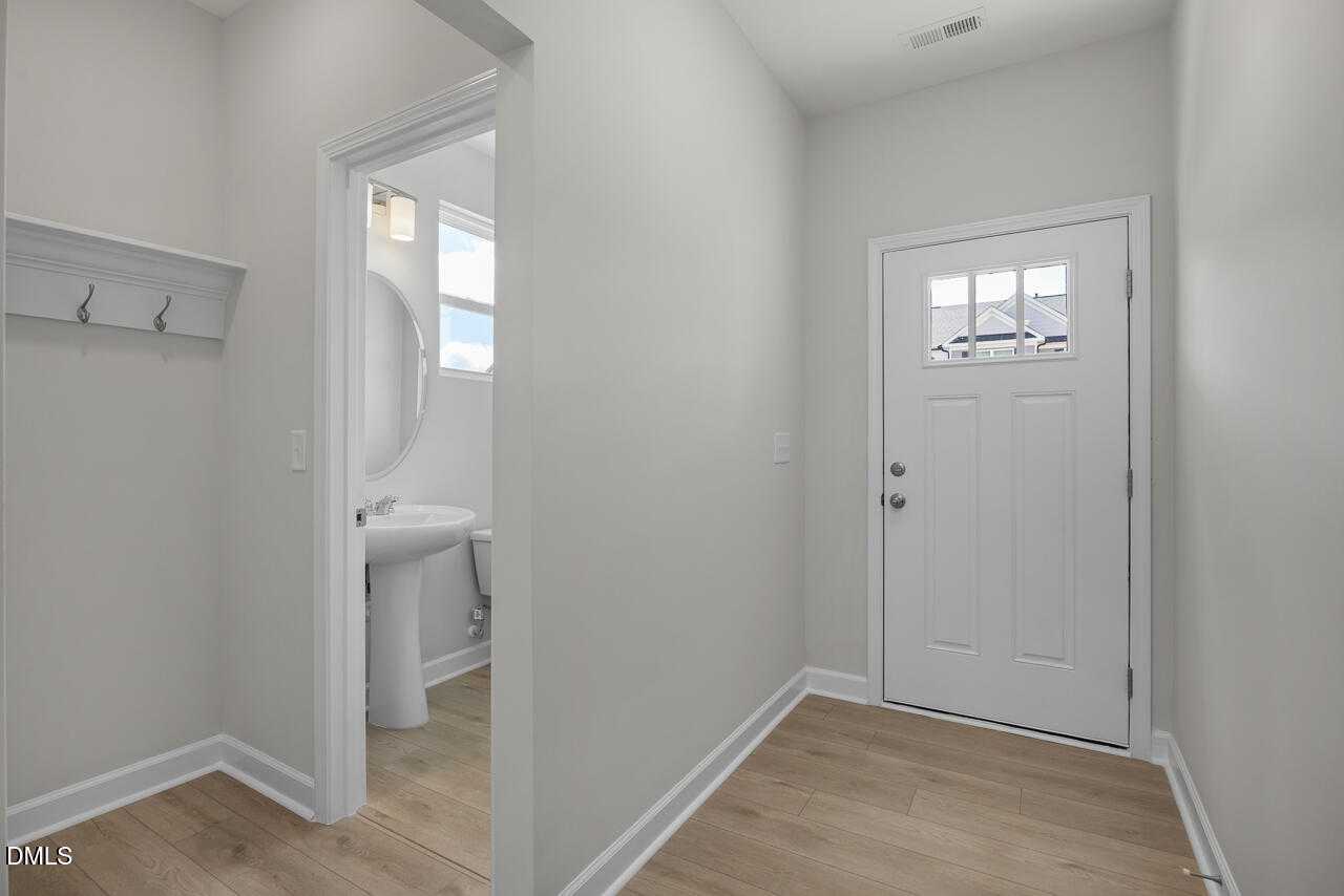 Bright entryway with coat hooks, white front door, and adjacent powder room with pedestal sink in Davidson Homes The Graham, Fuquay-Varina, NC