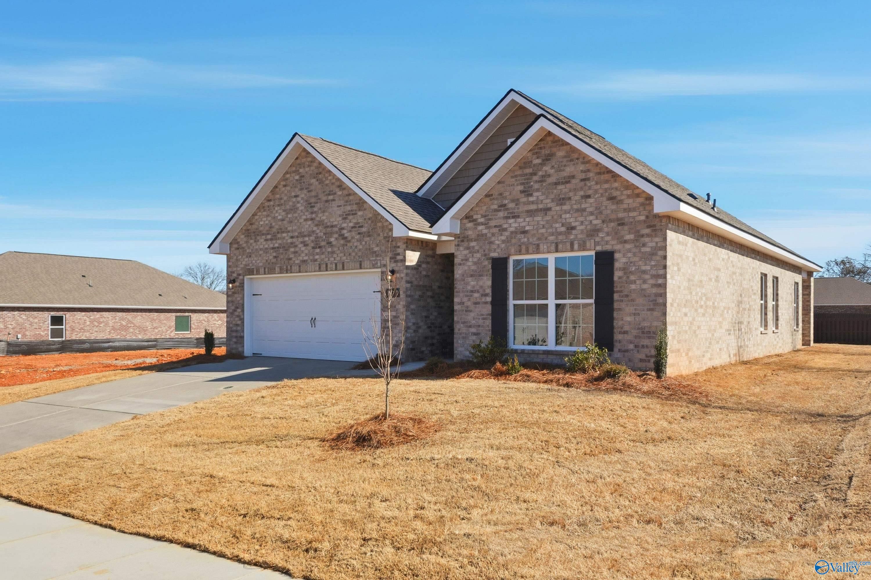 Brick ranch home with light brick facade, 2-car garage, driveway, and young tree in Flint Meadows, New Market, Alabama