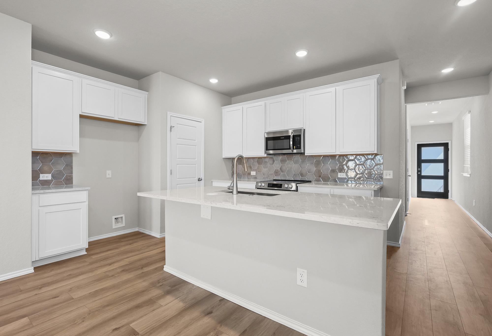 Modern kitchen in The Colorado B featuring white cabinets, quartz countertops, and a stylish hexagonal tile backsplash.