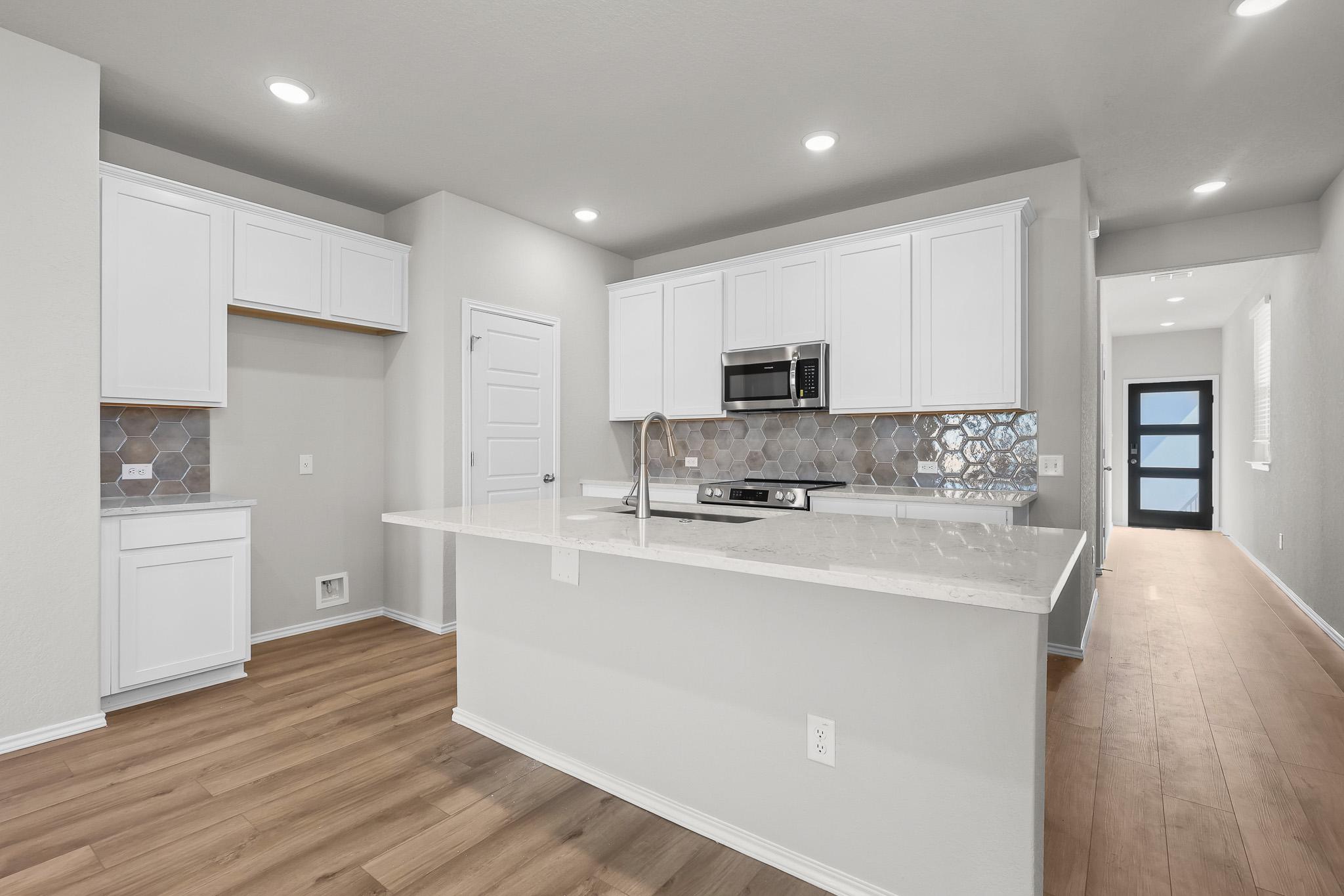 Modern kitchen in The Colorado B featuring white cabinets, quartz countertops, and a stylish hexagonal tile backsplash.
