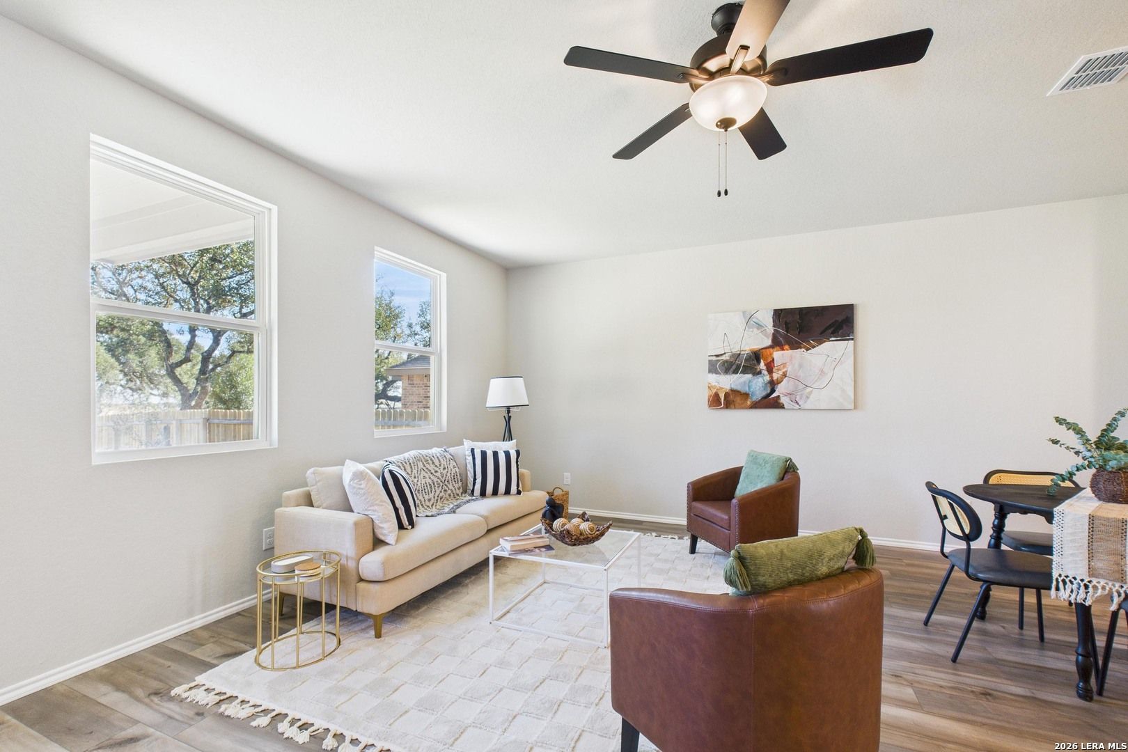 Cozy living room with beige sofa, leather armchair, ceiling fan, and dining area in 4-bedroom Davidson Homes The Douglas E, Bricewood, San Antonio