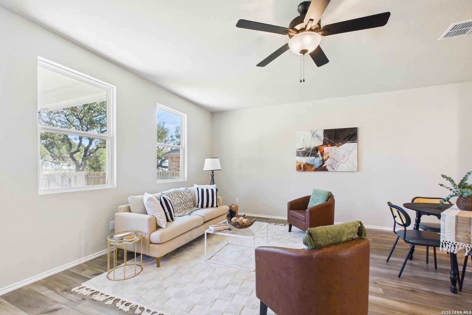 Cozy living room with beige sofa, leather armchair, ceiling fan, and dining area in 4-bedroom Davidson Homes The Douglas E, Bricewood, San Antonio