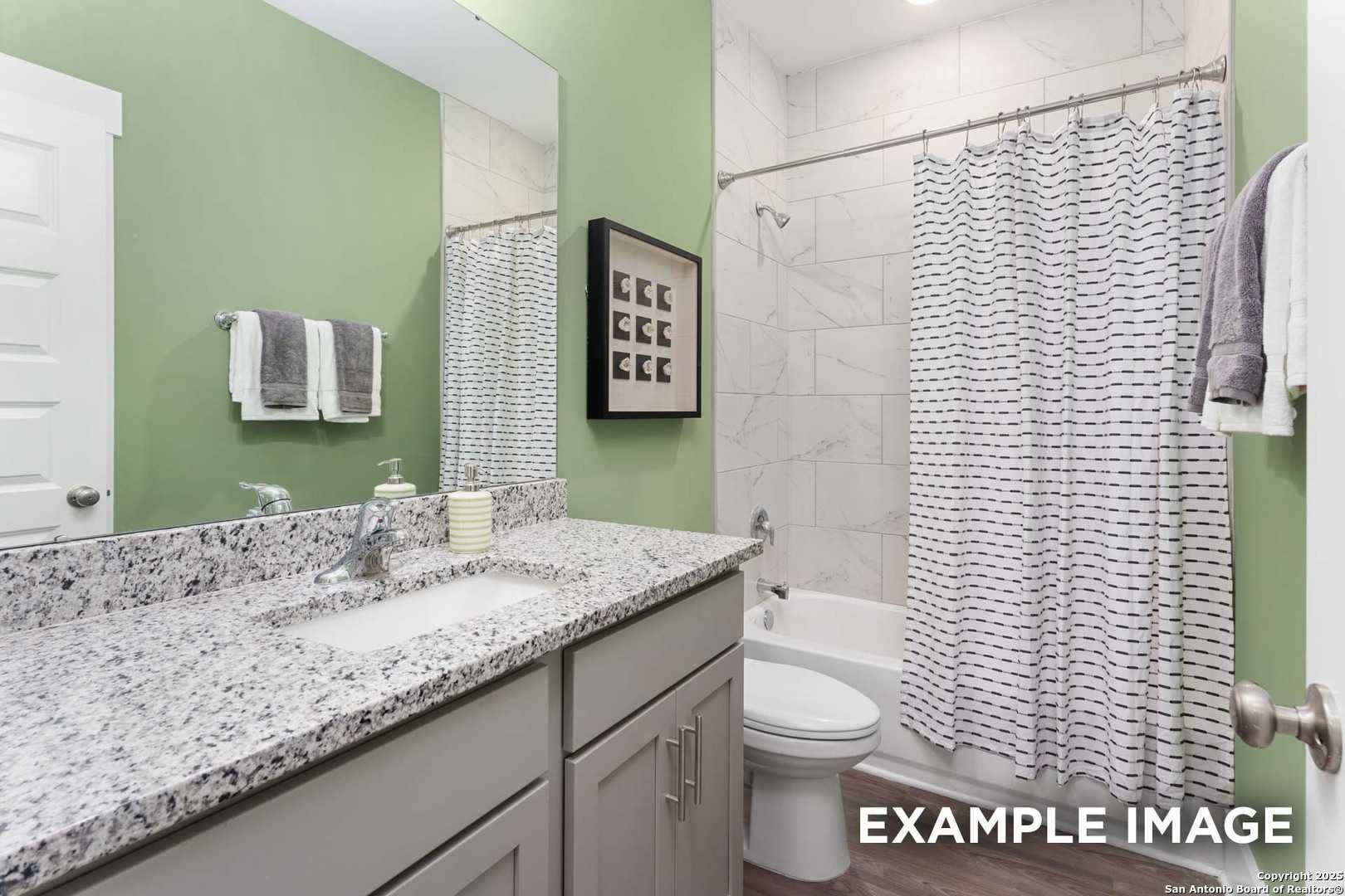 Bright secondary bathroom with sage green walls, granite vanity, and tub shower in Davidson Homes The Daphne H, Seguin, Texas