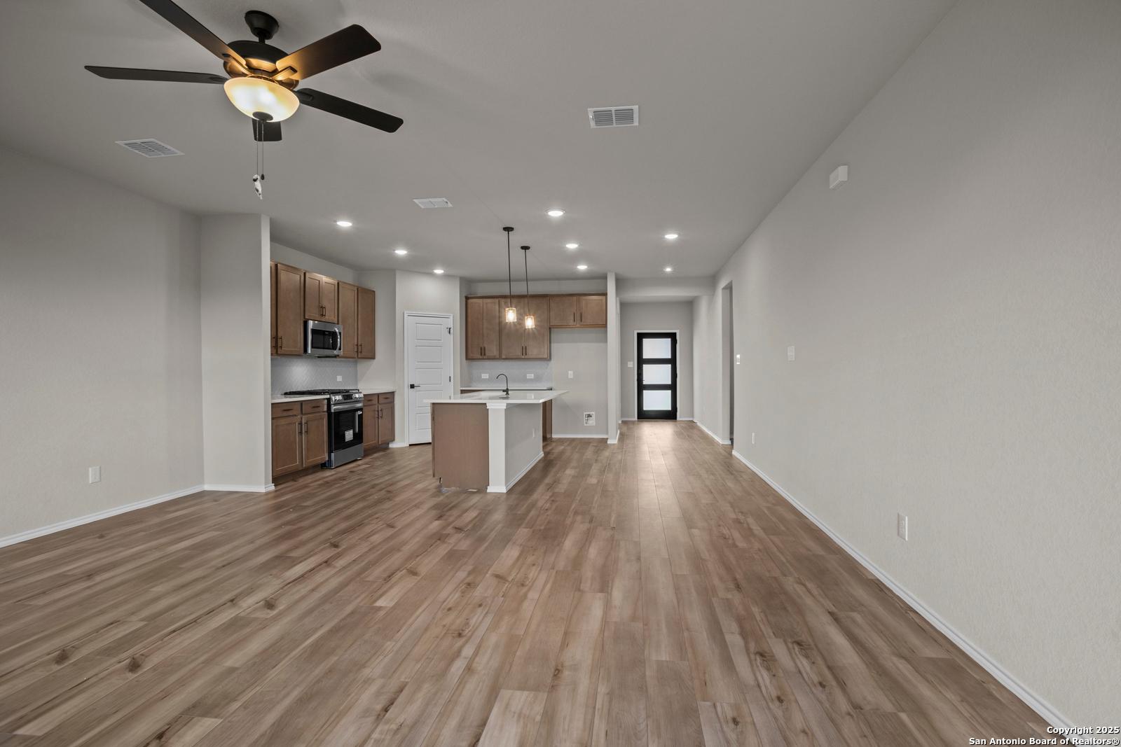 Spacious open kitchen-living area with hardwood floors, island, ceiling fans, and glass door in Davidson Homes Douglas F, San Antonio