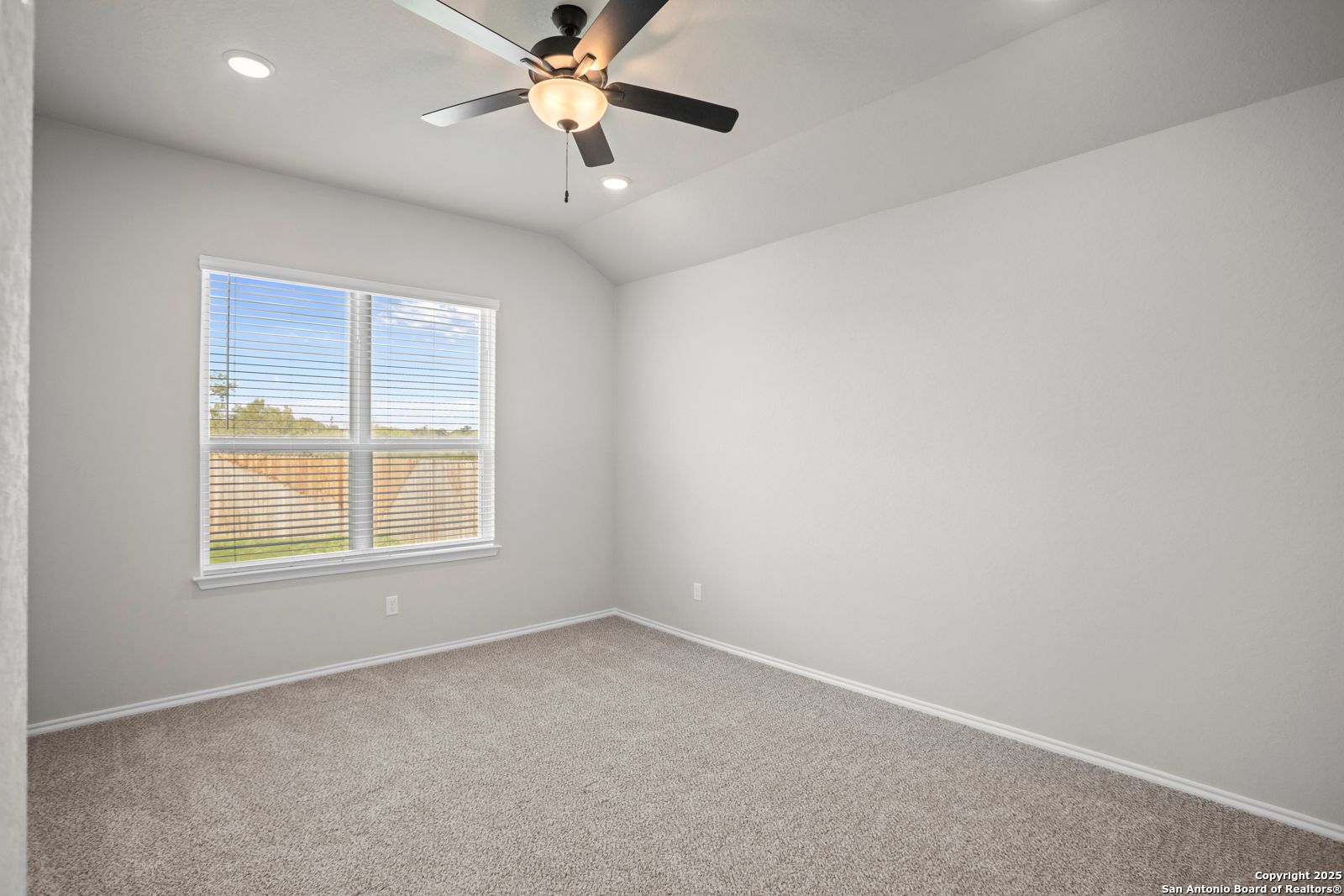 Bright bedroom with gray walls, beige carpet, ceiling fan, and large window overlooking fenced yard in Davidson Homes Sequoia A, Converse TX