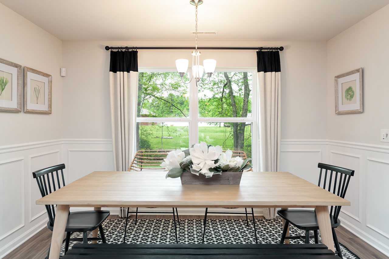 Spacious dining room in The Franklin home with oak table, black chairs, bench seating, white floral centerpiece, chandelier, and window view of greenery