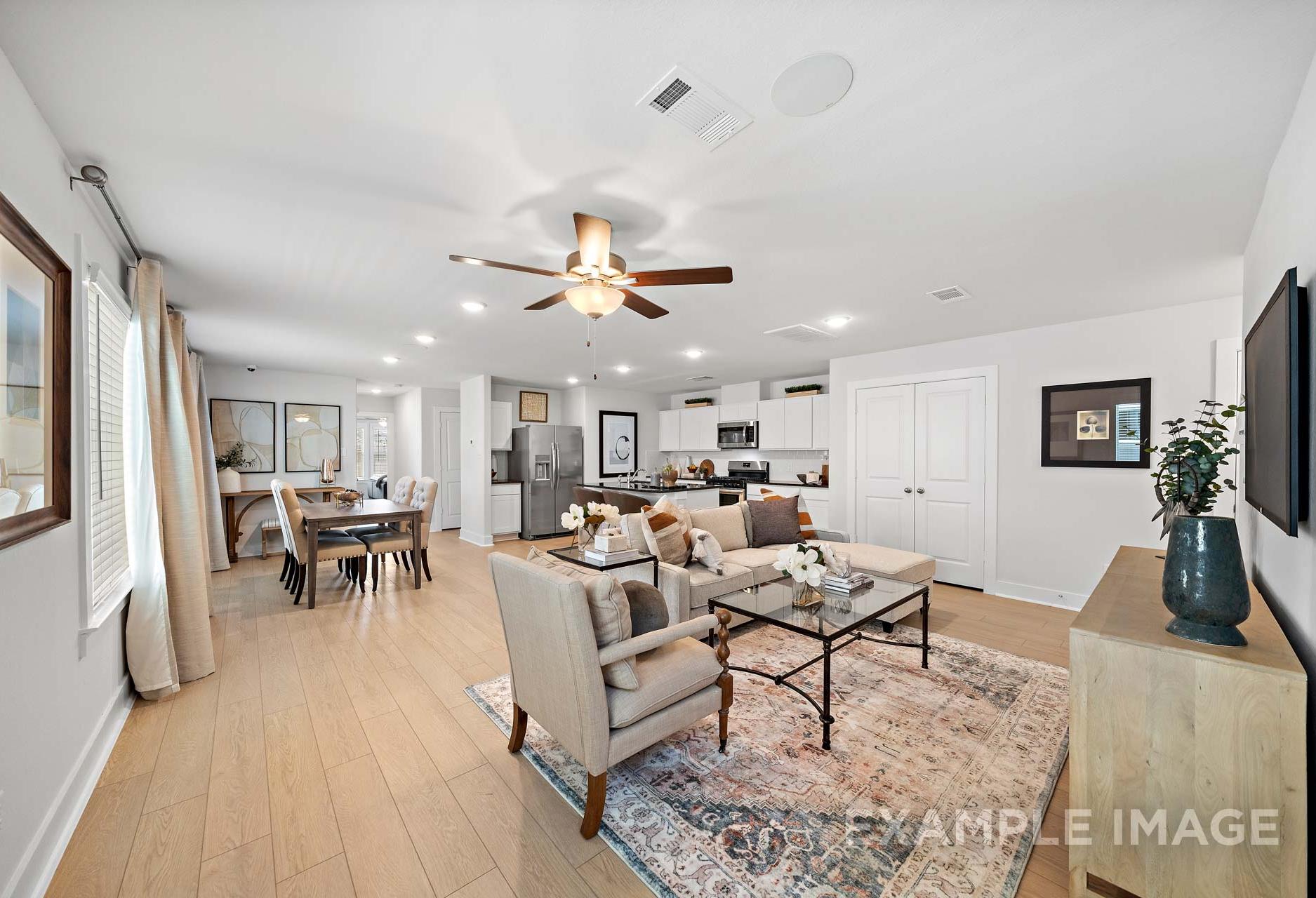 Spacious open-concept living room and kitchen in The Rose B, featuring hardwood floors, white cabinetry, dining table, and ceiling fan
