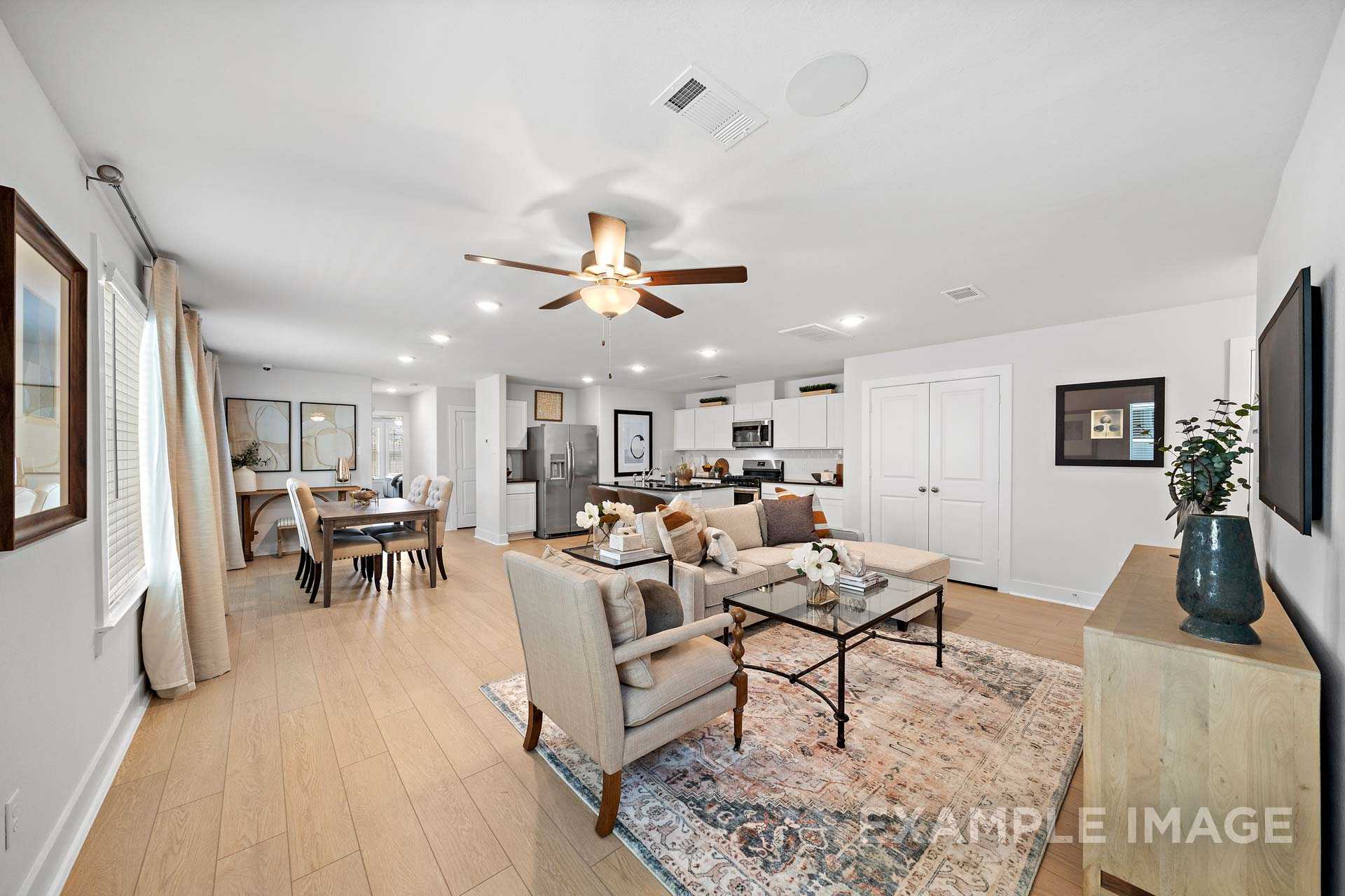 Spacious open-concept living room and kitchen in The Rose B, featuring hardwood floors, white cabinetry, dining table, and ceiling fan