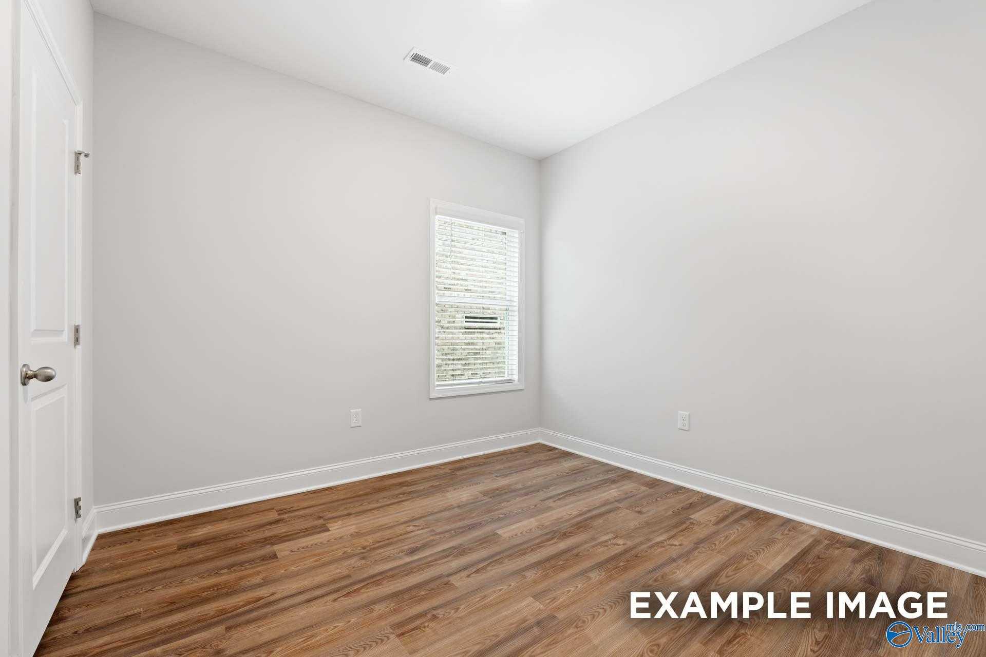 Bright secondary bedroom with light gray walls, hardwood floors, and window blinds in Davidson Homes The Cumberland, Decatur, Alabama