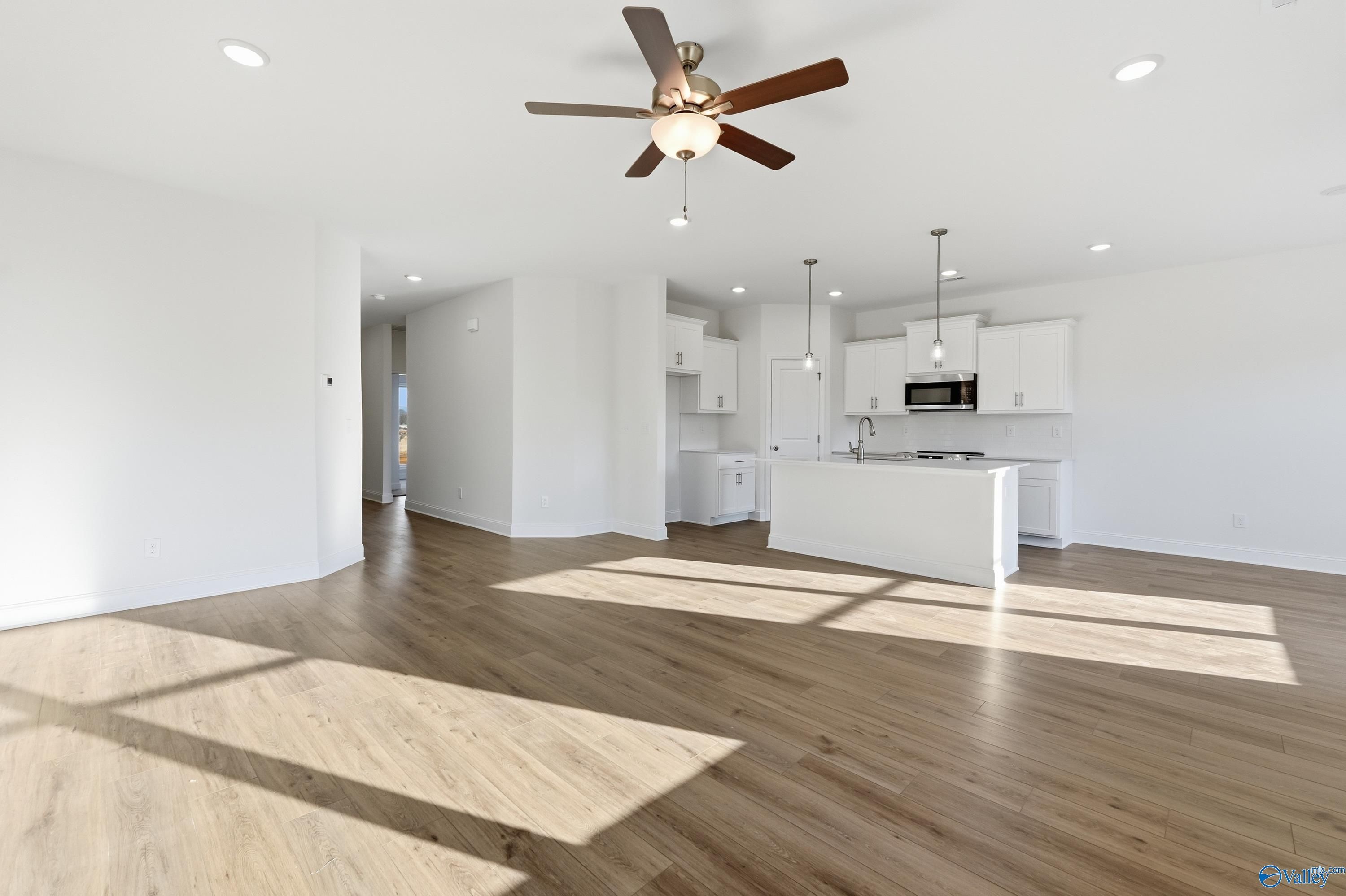 Sunlit open kitchen with white cabinets, island, hardwood floors, and ceiling fan in Davidson Homes Asheville C, Meridianville, AL