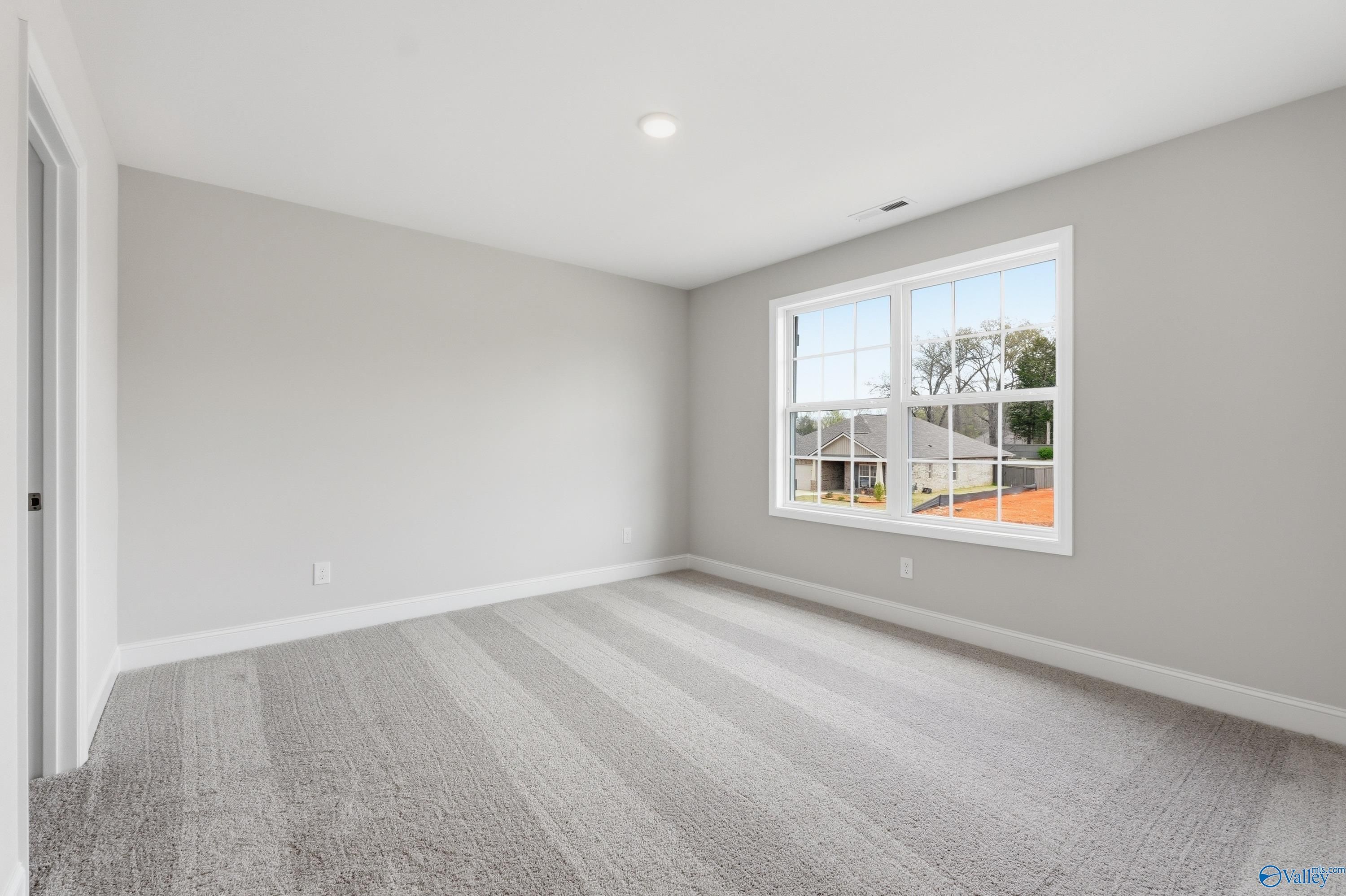 Spacious empty bedroom with gray walls, striped carpet, and window view in The Shelby B, Davidson Homes, New Market, Alabama