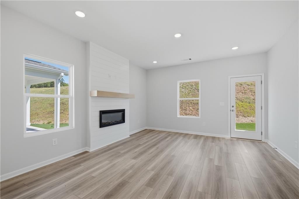 Bright great room with shiplap fireplace accent wall, wood-look flooring, and rear entry door in Davidson Homes' The Oconee B, Canton, GA